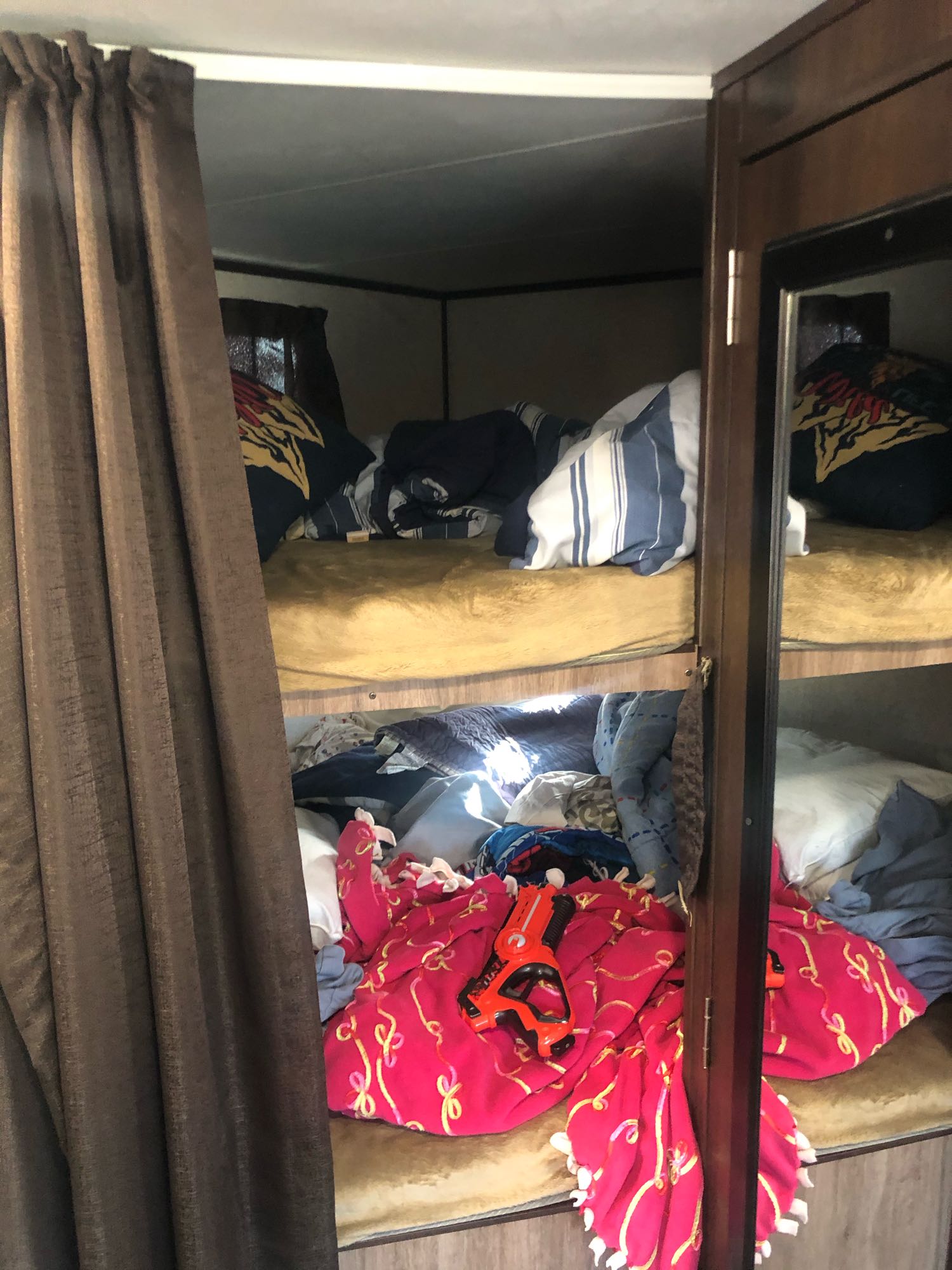 An RV rental's cozy, yet cluttered, bunk beds. Blankets, pillows, and a toy blaster fill the sleeping area.. Jayco Jay Feather 2018