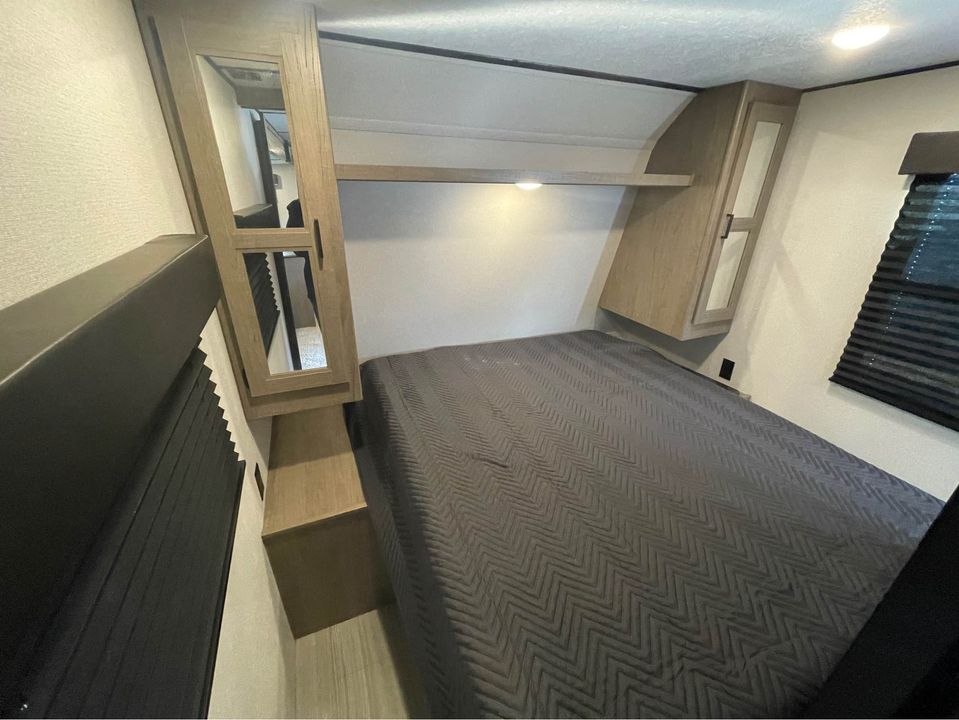 RV rental sleeping area: compact bedroom with bed, built-in mirrored cabinet, and window for travel.. Keystone Other 2021
