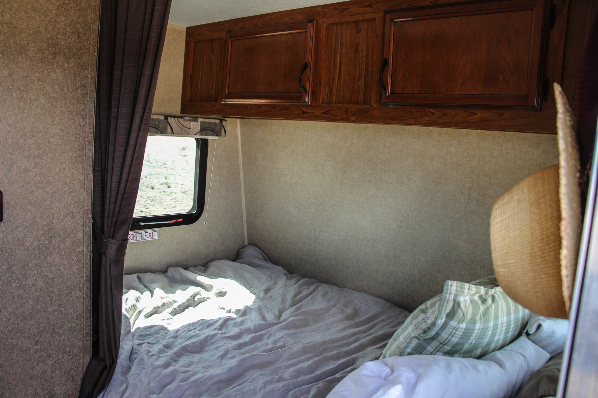 Cozy RV rental interior: a bedroom with sunlight on the bed, a window, and overhead cabinets for storage.. Starcraft Launch 2015