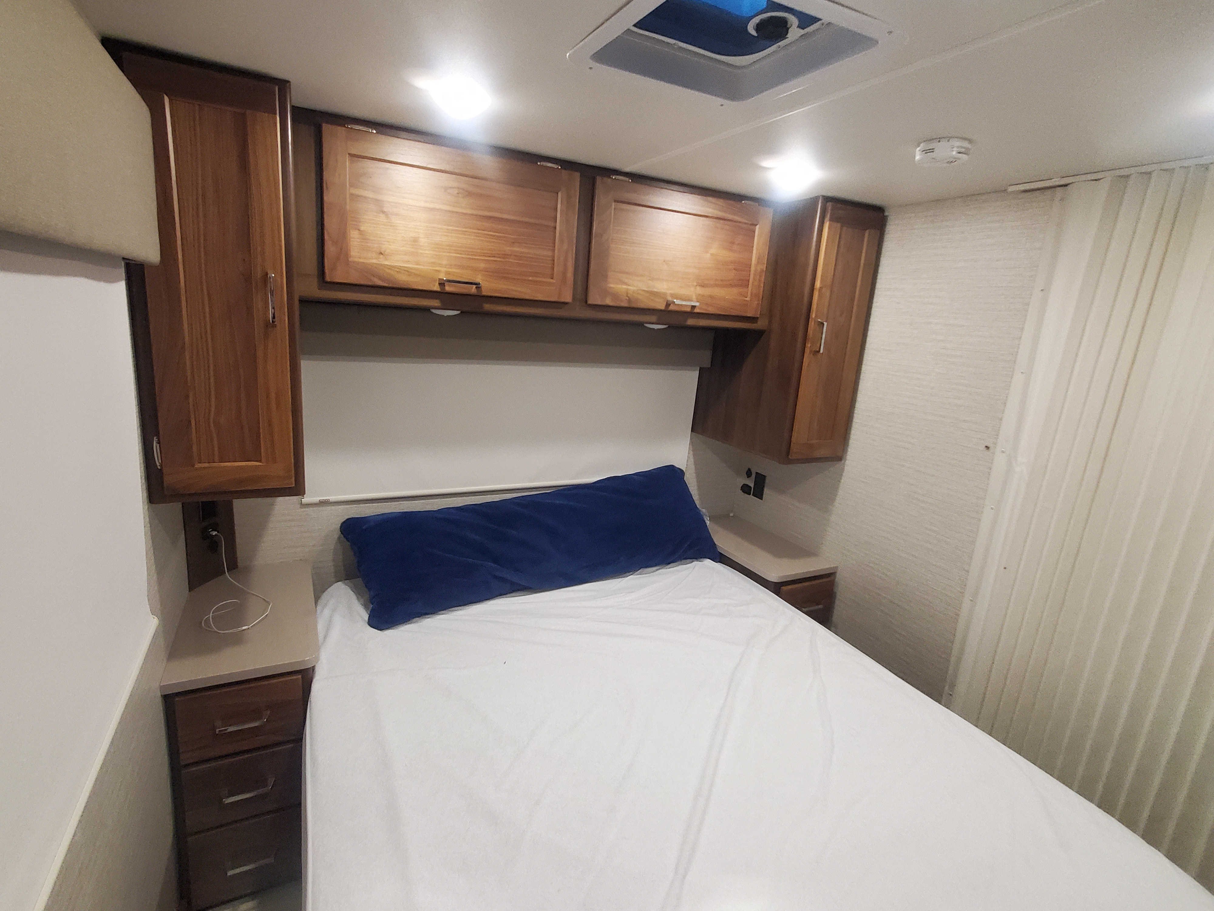 Cozy RV rental bedroom with wood cabinets, bedside charging, and white sheets, ideal for compact travel.. Winnebago Minnie Winnie 2021