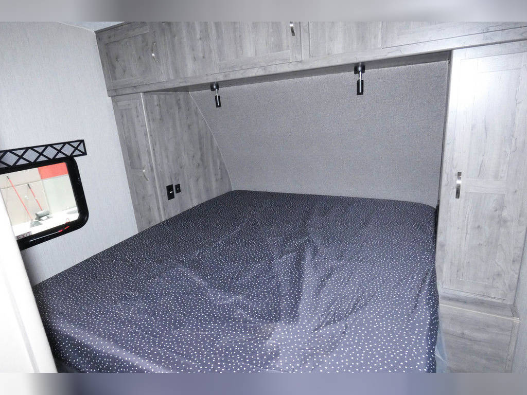RV rental bedroom features a comfortable bed with overhead cabinets, wardrobe, and window. Light gray walls and wood-look finishes.. Forest River Work And Play 2021