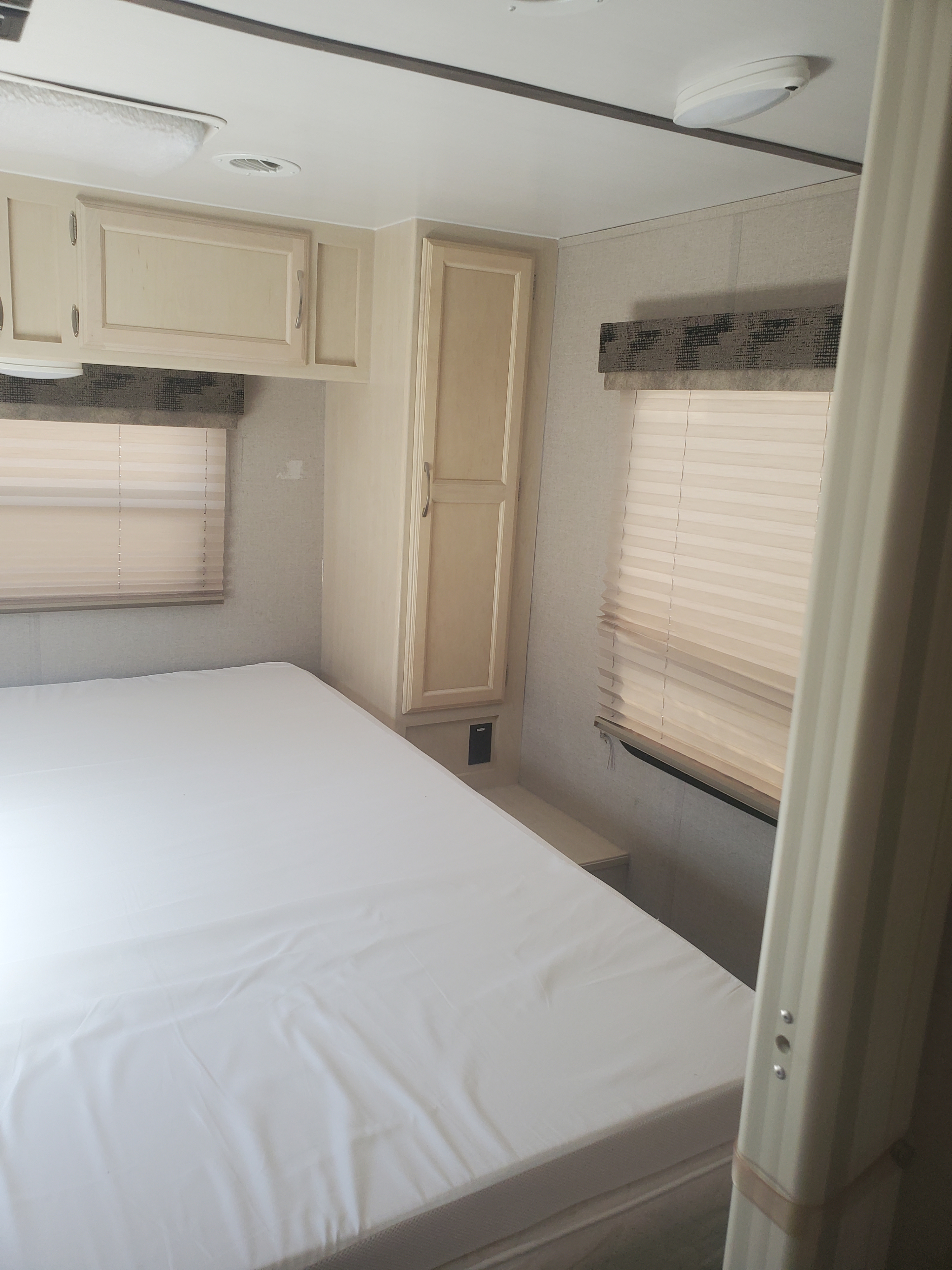 RV rental interior: A bright, clean bedroom with a bed, overhead cabinets, and a window with blinds.. Other Other 2019