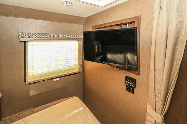 Cozy RV rental bedroom with a comfortable bed, window with blinds, and wall-mounted TV for entertainment on the go.. Thor Motor Coach Freedom Elite 2019