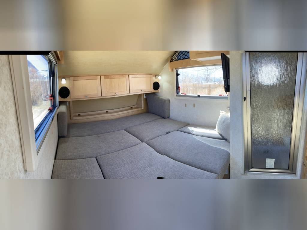 Cozy RV rental interior with a convertible bed, wood cabinetry, and large windows. Ideal for comfortable travel.. nucamp t@b 2019