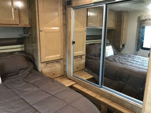 Cozy RV rental bedroom with two comfortable beds, wood cabinets, and mirrored sliding wardrobe for storage.. Coachmen Leprechaun 2018