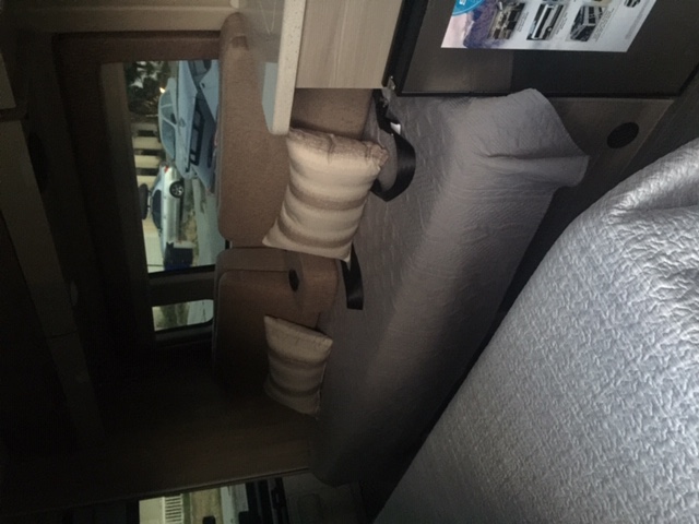 An RV rental's interior: a comfortable bed and seating area with a window view of parked vehicles outside.. Thor Sequence 2021