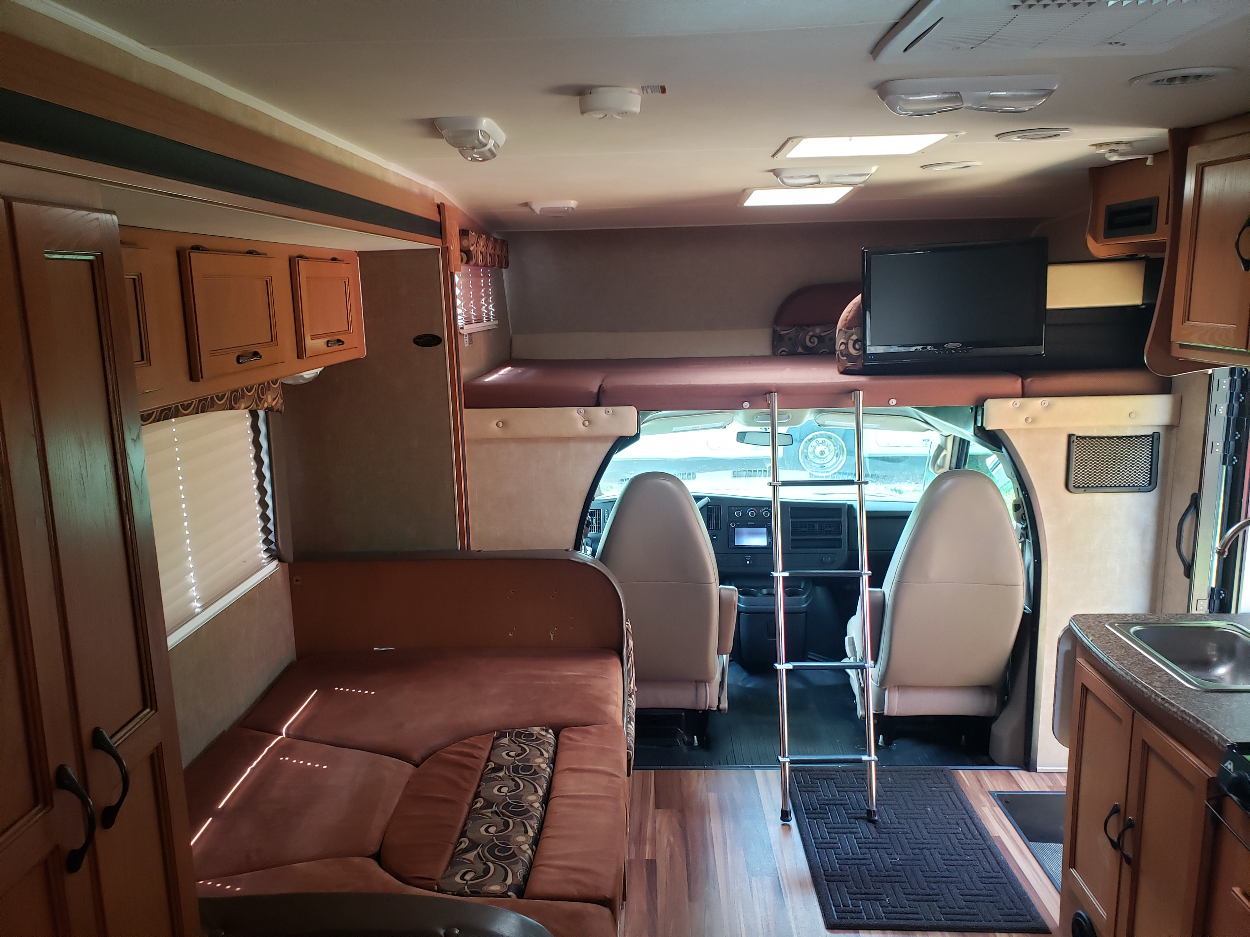 RV rental interior: convertible sofa bed, over-cab bunk with TV, kitchen, and driver's cockpit.. Coachmen Freelander 2013