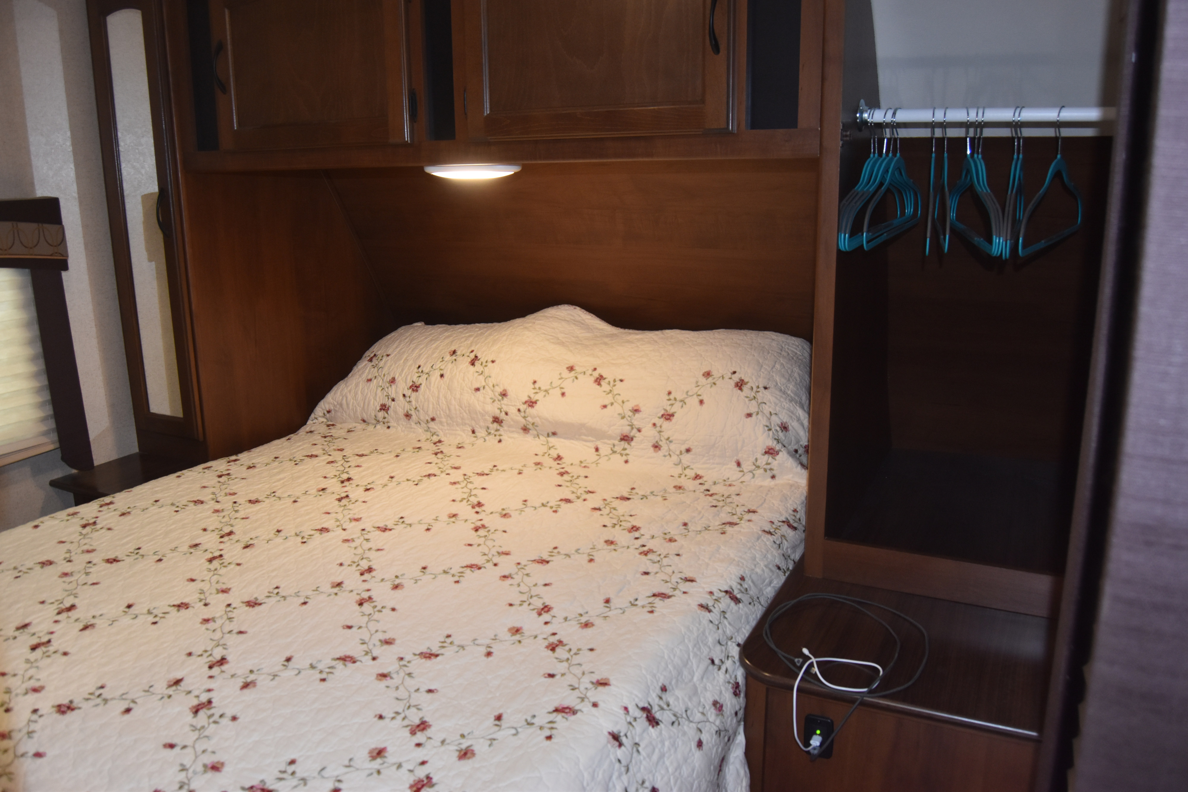 Cozy RV rental bedroom: white floral bed, wood cabinets, closet with hangers, charging port.. Jayco White Hawk Ultra Lite 2015