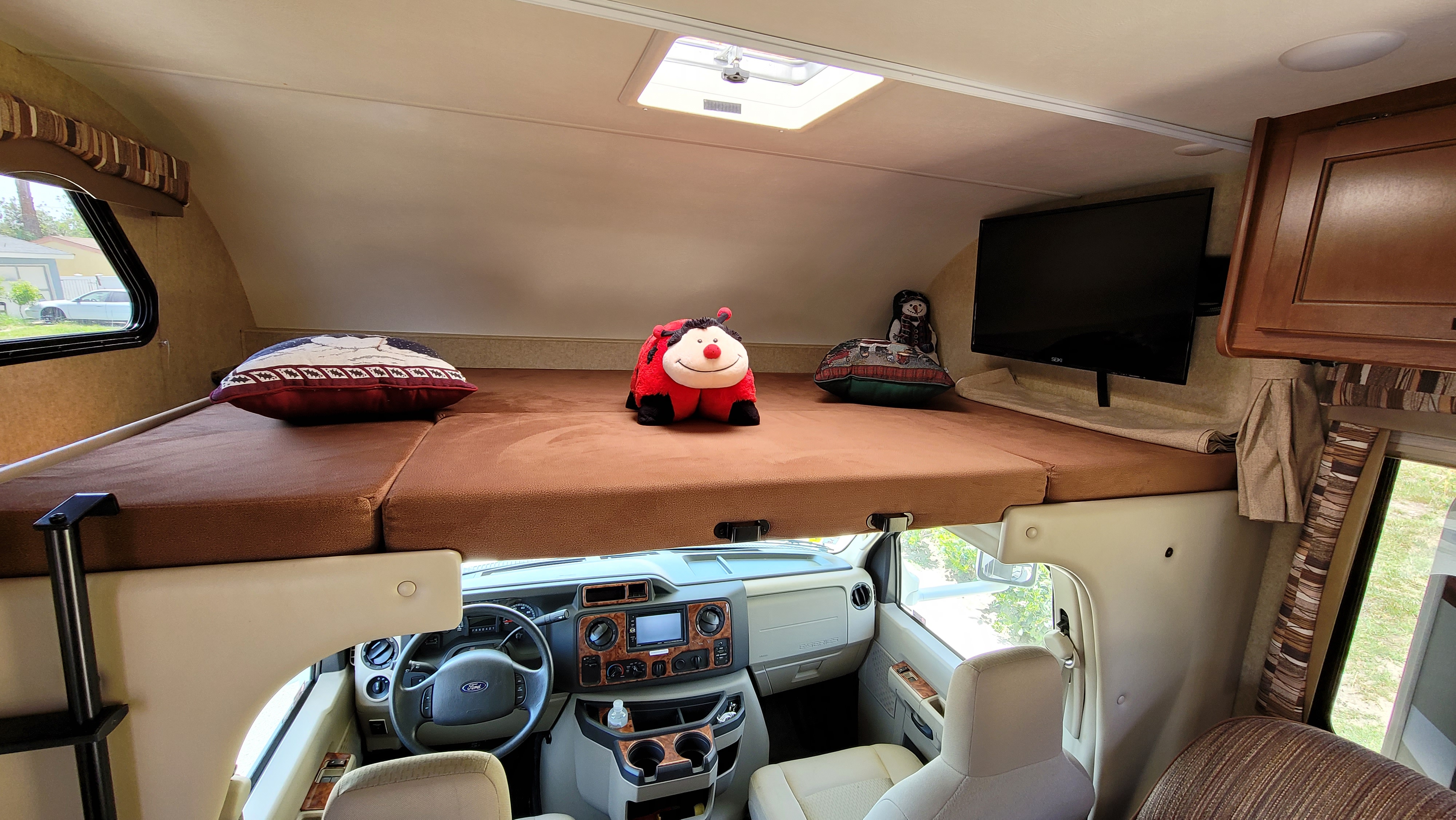 Inside an RV rental, featuring a cozy overhead bunk bed with pillows and a ladybug plush, plus the driver's cabin below.. Thor Motor Coach Chateau 2016
