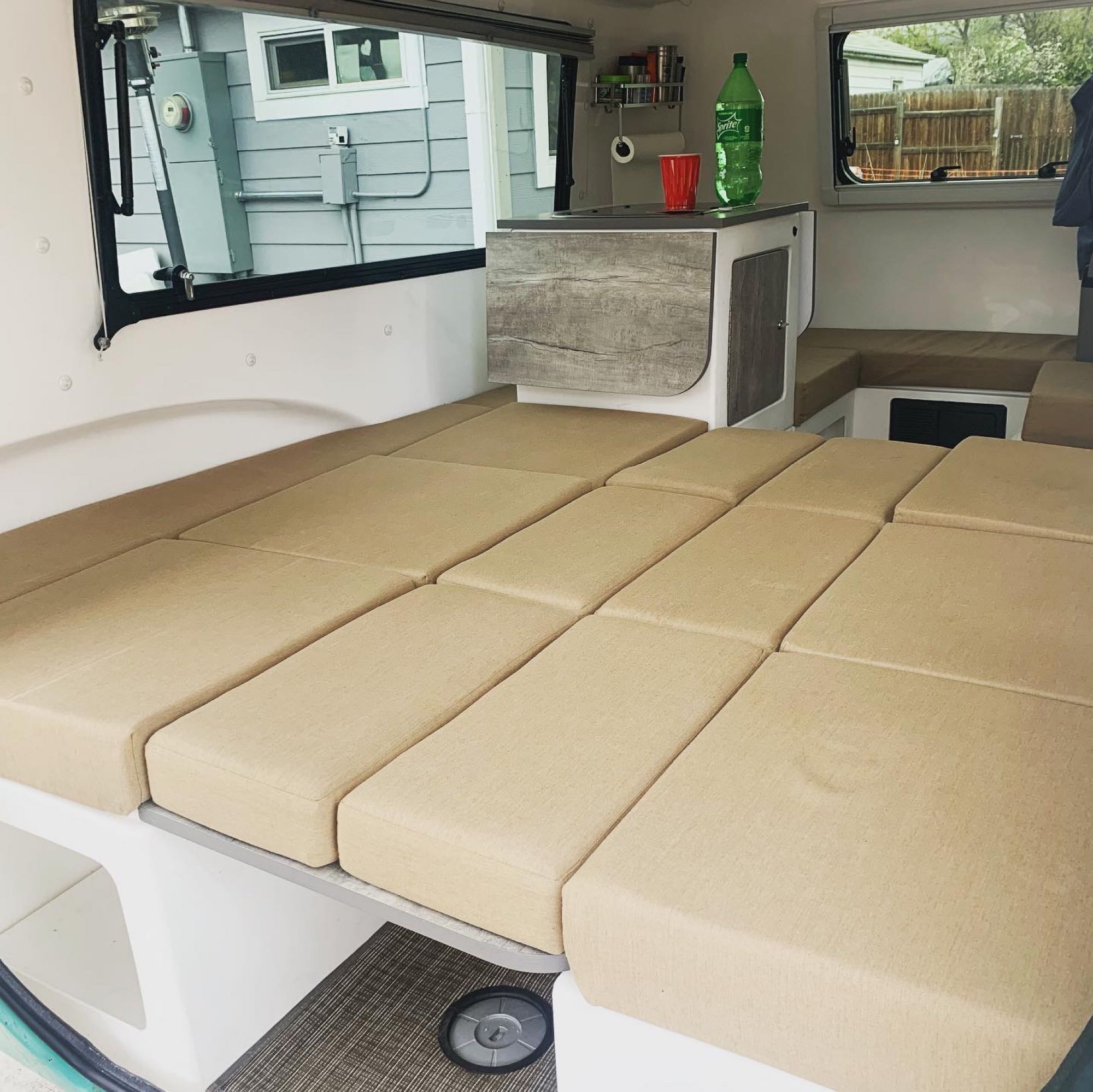 Versatile beige cushioned lounge area/bed in an RV rental, complete with a compact kitchen counter, ideal for travel.. Happier Camper HC1 2020