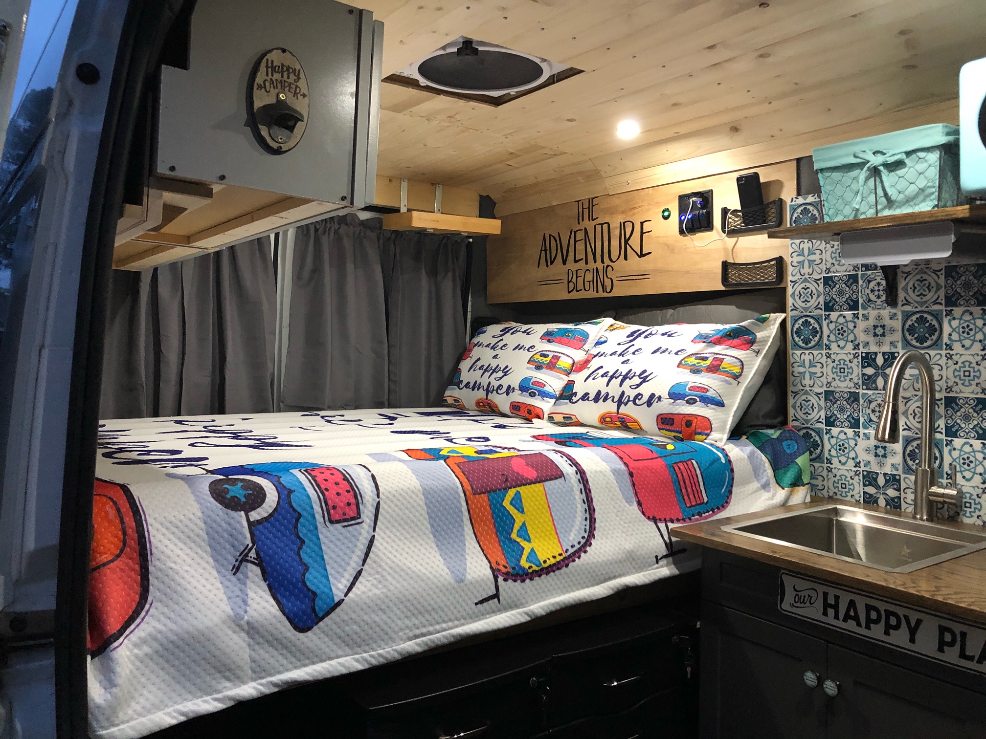 Step inside this charming RV rental! A cozy camper van interior with a bed, kitchen sink, and "The Adventure Begins" decor.. Dodge Ram 1500 2019
