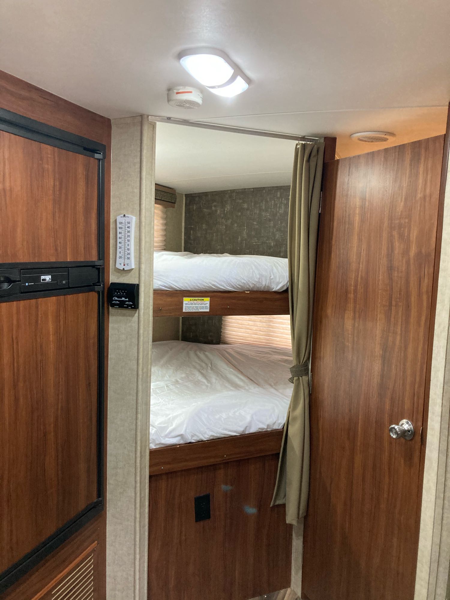 This RV rental interior features bunk beds with white linens, a compact refrigerator, and a wall thermometer. Ideal for travel.. Heartland North Trail 2015
