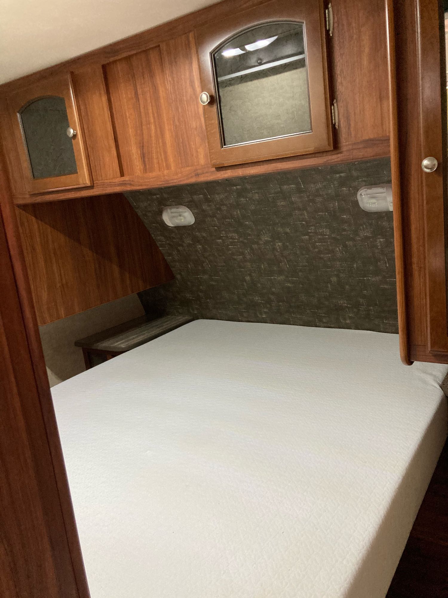 RV rental bedroom featuring a clean white mattress, rich wooden cabinets, and convenient overhead lighting.. Heartland North Trail 2015