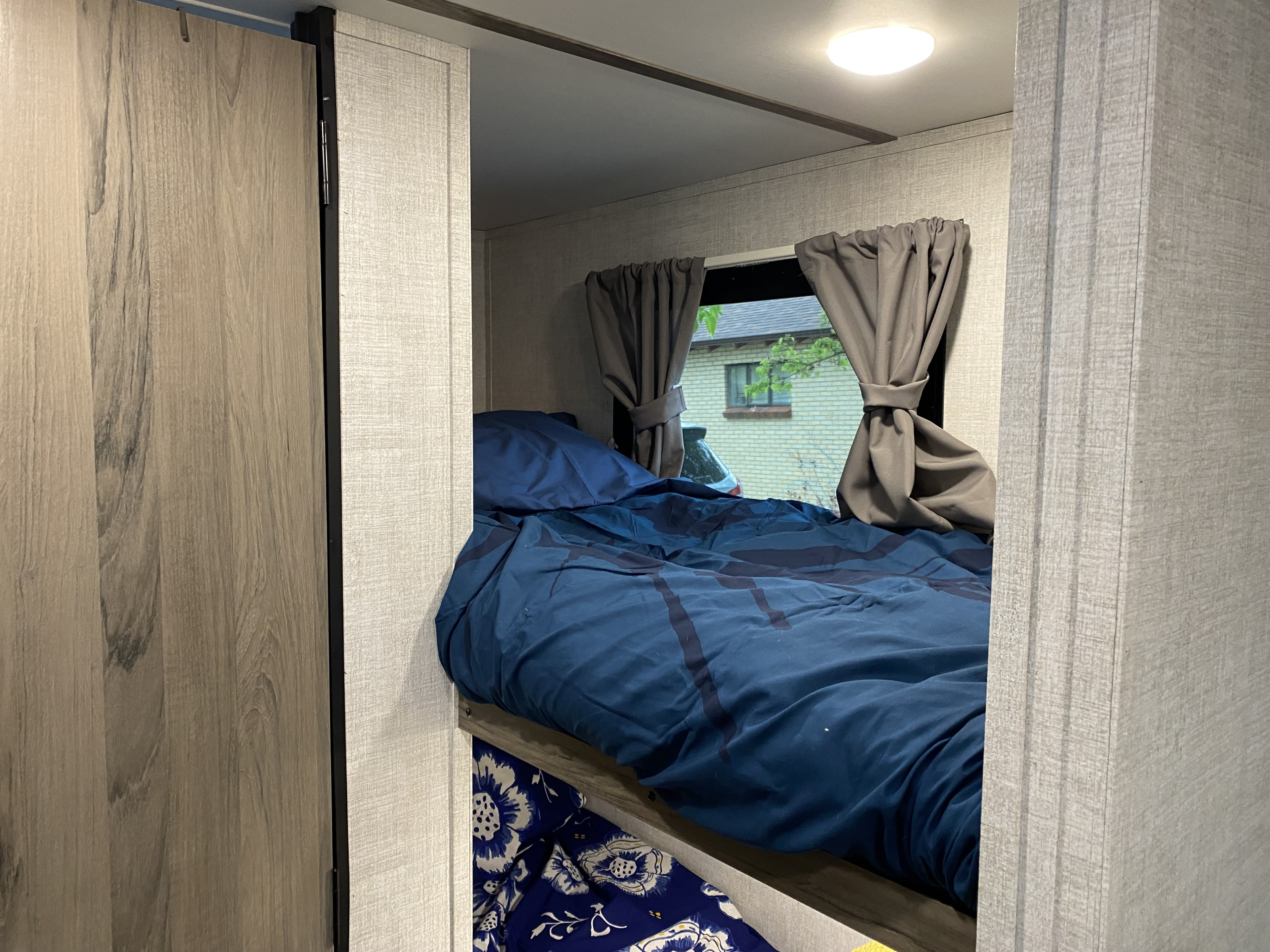 Inside an RV rental: a neat upper bunk with blue bedding and a window view, ideal for a cozy trip.. Gulf Stream Amerilite 2021
