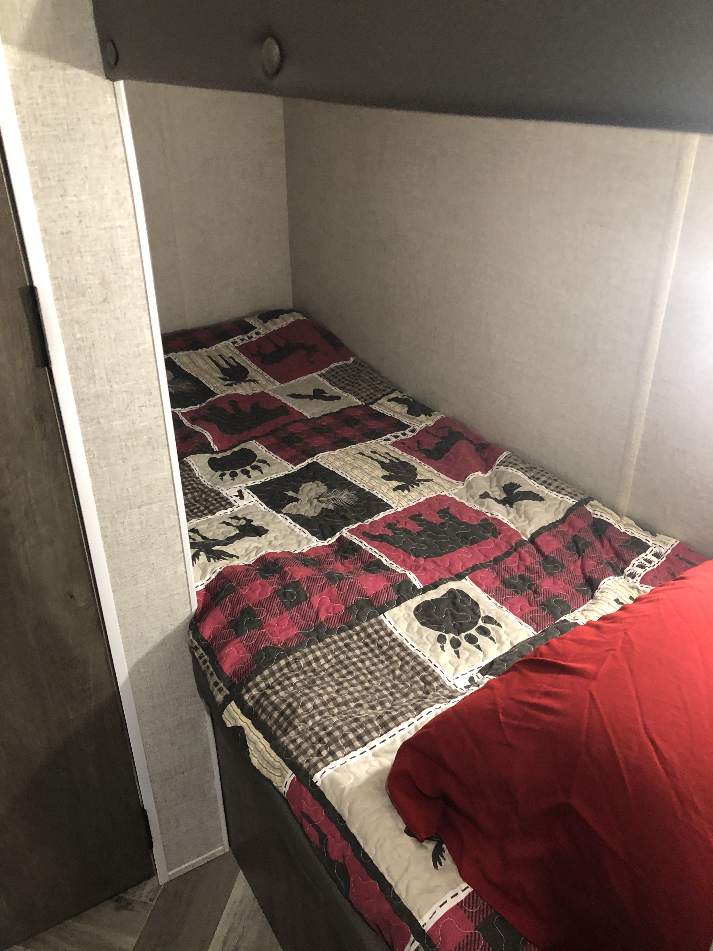 A single RV rental bunk bed with a cozy woodland-themed comforter and red blanket, ready for your adventure.. Forest River Salem Cruise Lite 2021