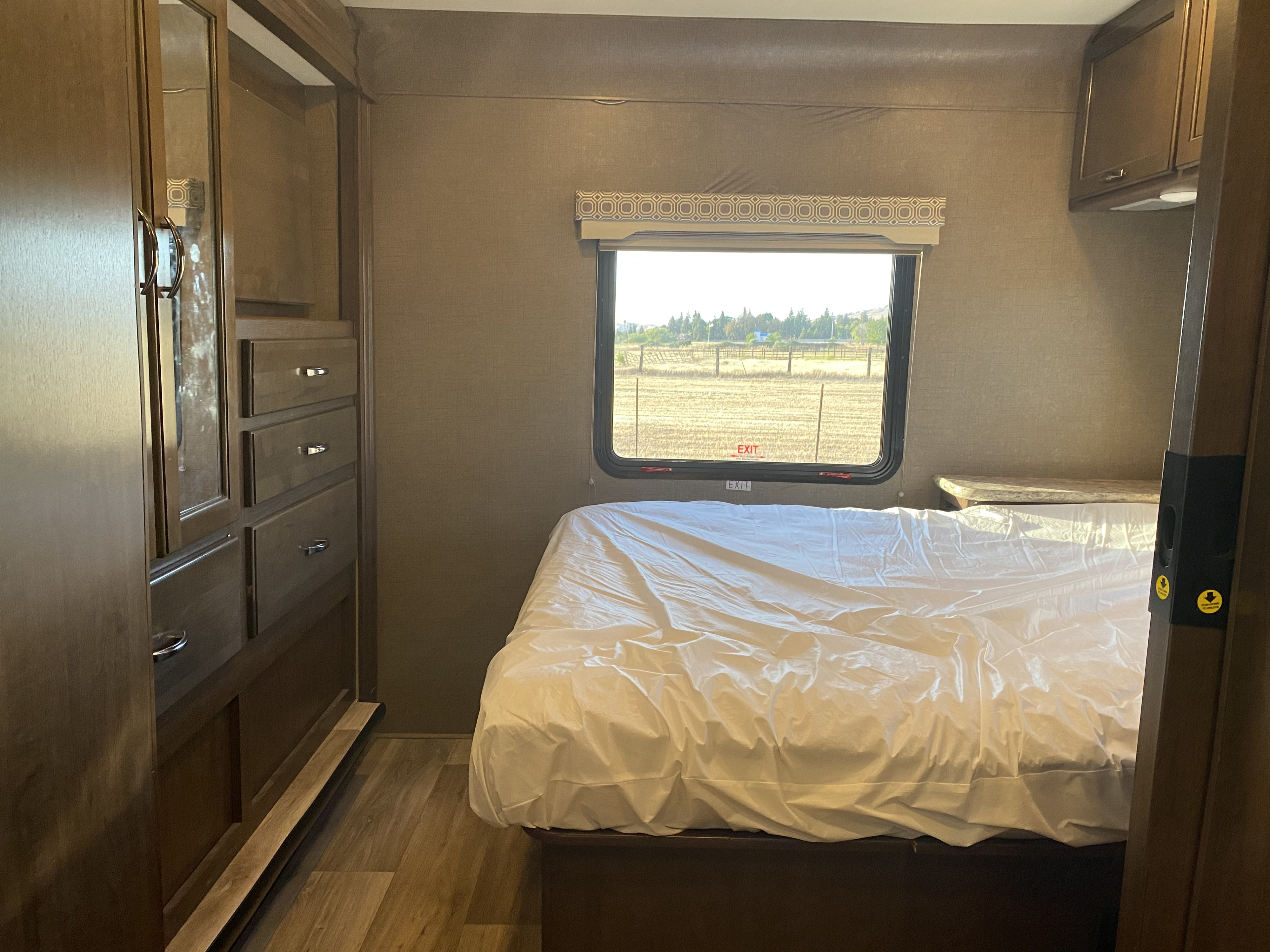Experience an RV rental: a cozy bedroom with a white-sheeted bed, wardrobe, and window to a scenic field.. Thor Motor Coach Four Winds 2018