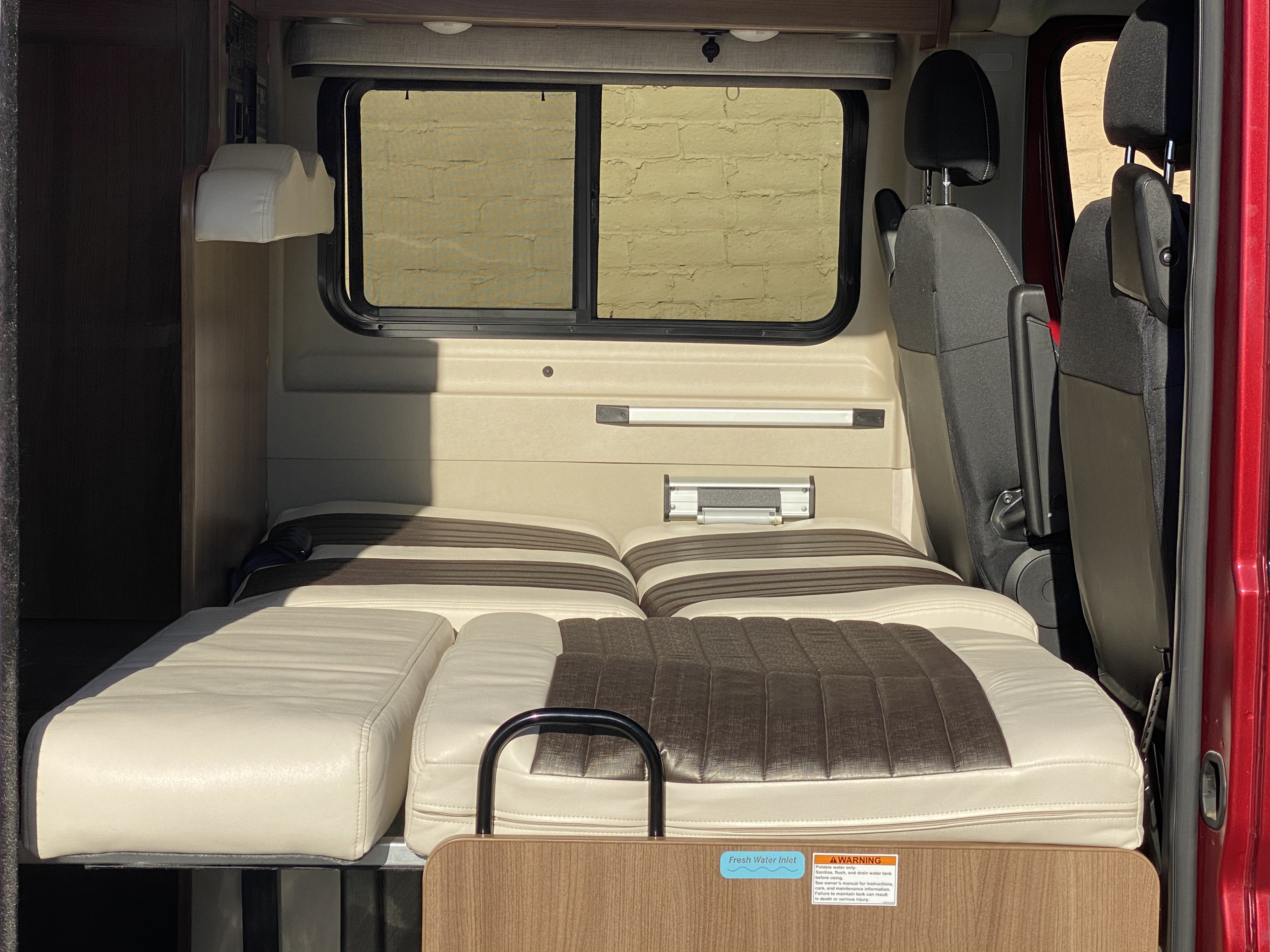 Interior of an **rv rental** camper van, featuring a multi-functional bed/seating area, window, and fresh water inlet connection.. Winnebago Travato 2018