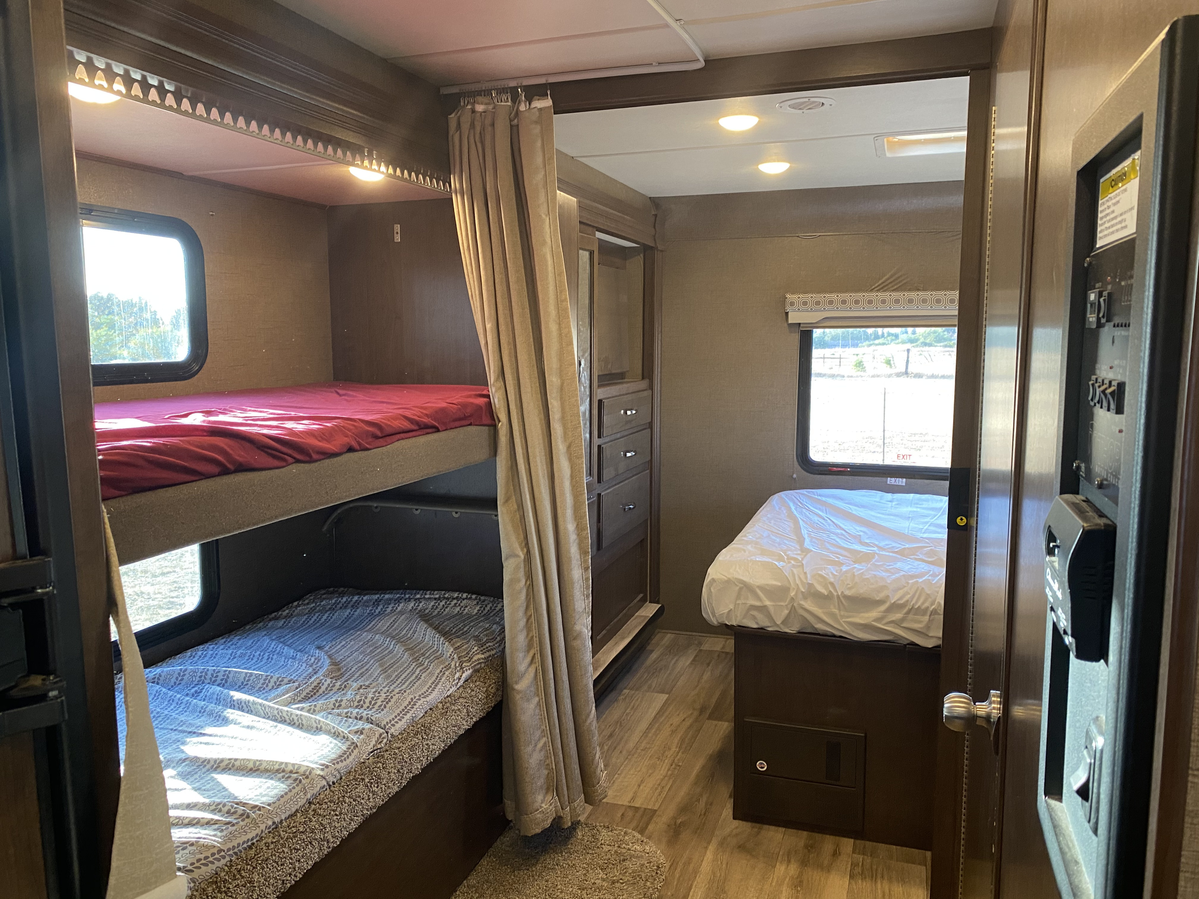 Bright RV rental interior with bunk beds (red & patterned sheets), a main bed, and dresser drawers.. Thor Motor Coach Four Winds 2018