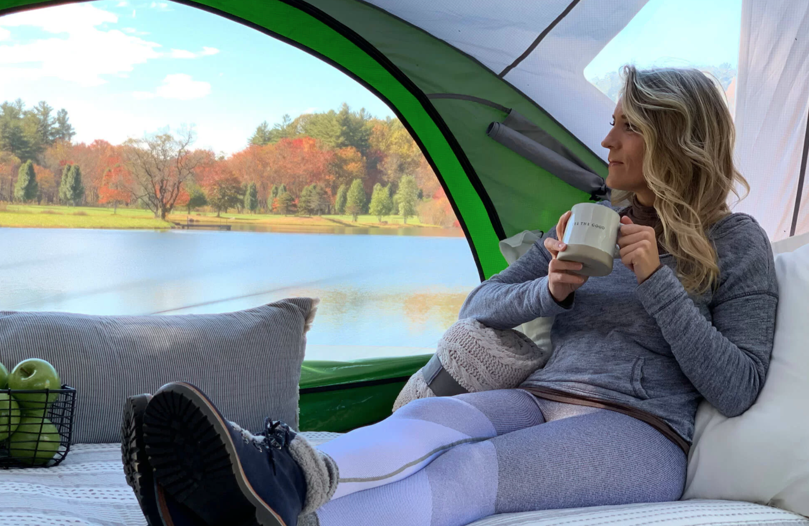 A woman relaxing in an RV rental setup, enjoying coffee & breathtaking autumn lake views from a cozy tent.. Other Other 2018