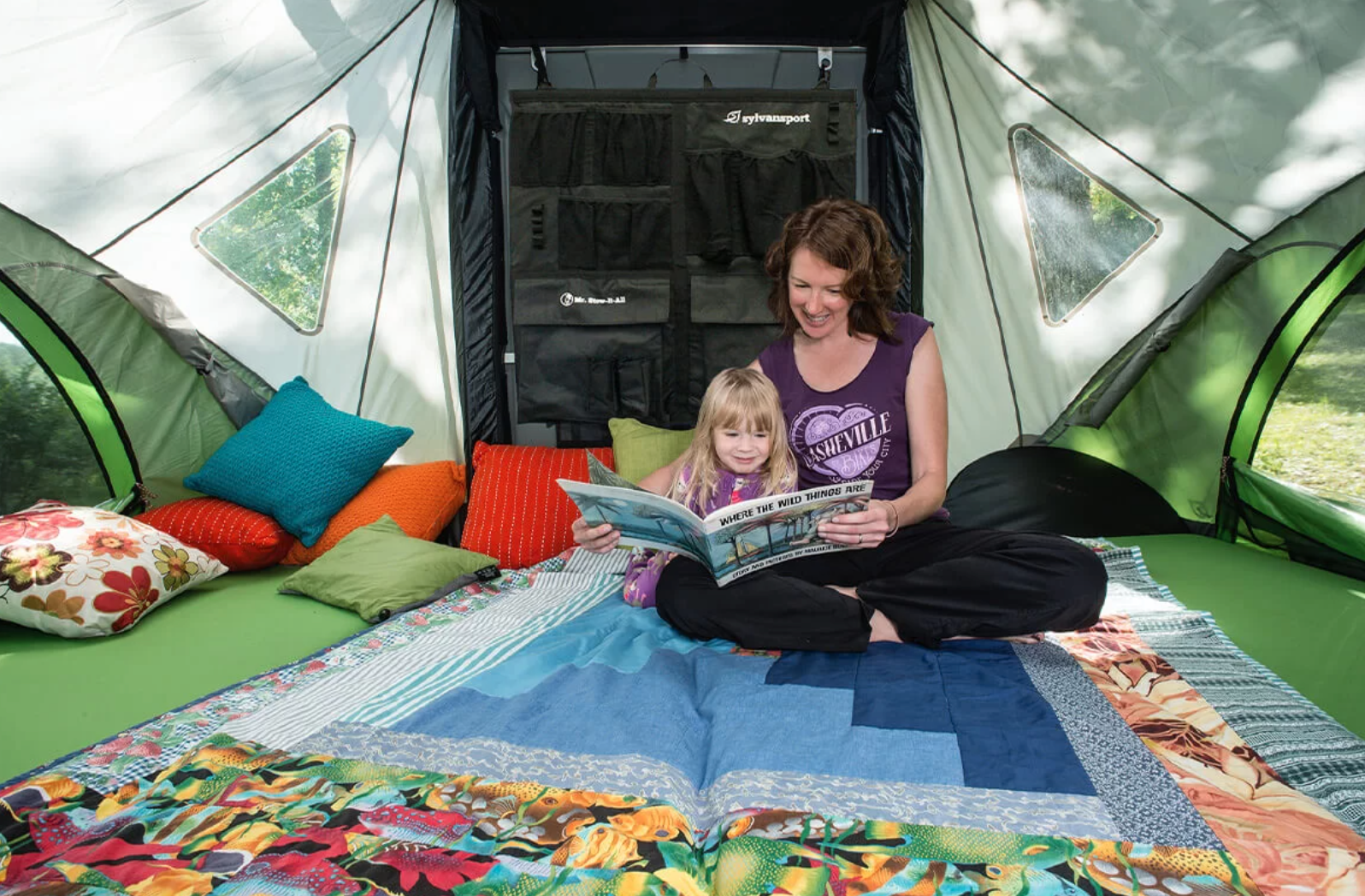 Cozy family moment inside an RV rental. A mother and child read a book surrounded by colorful pillows and blankets.. Other Other 2018