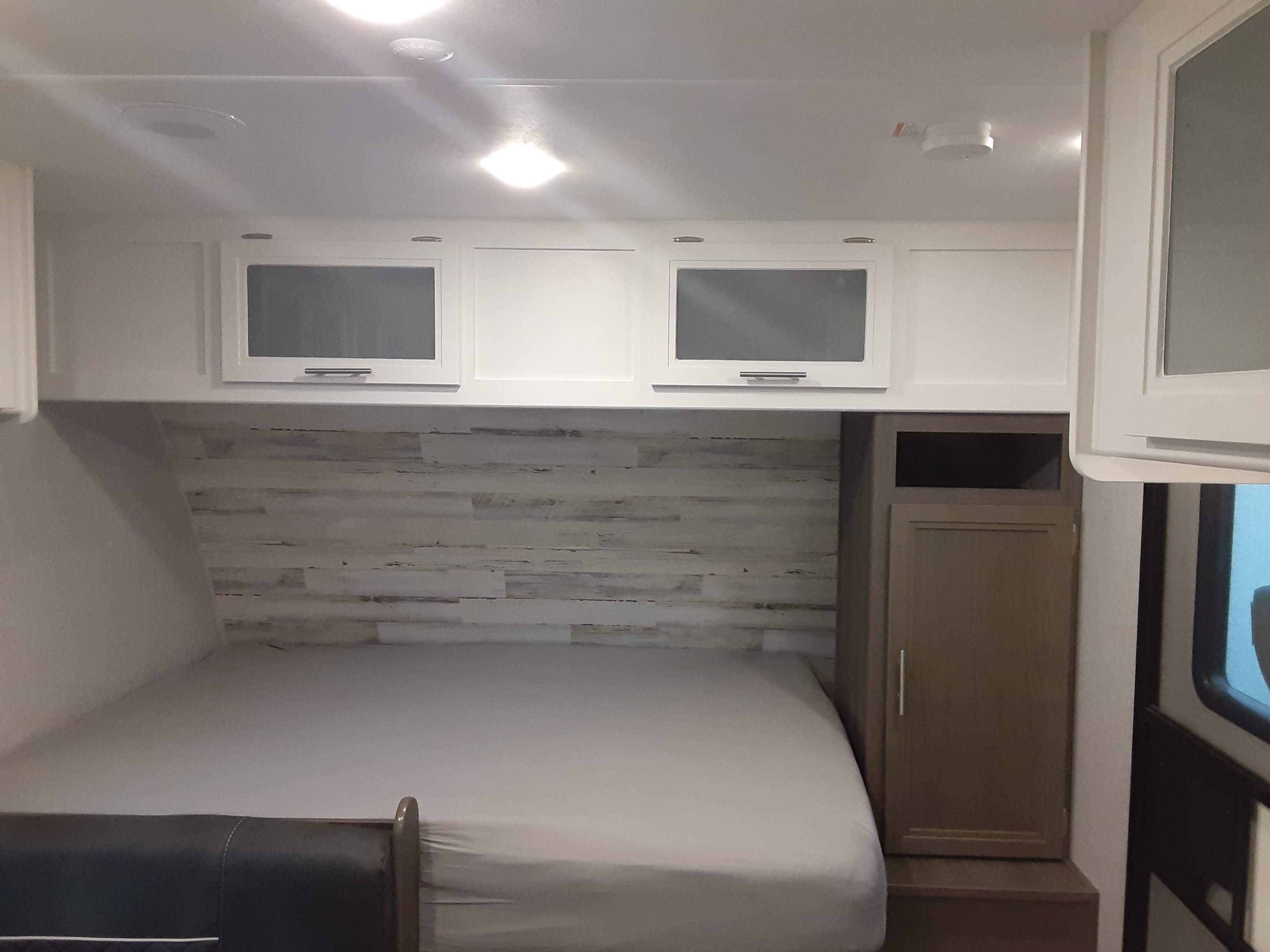 This RV rental offers a compact bedroom with a bed, wood-paneled wall, overhead white cabinets, and a wardrobe.. Dutchmen Kodiak 2021