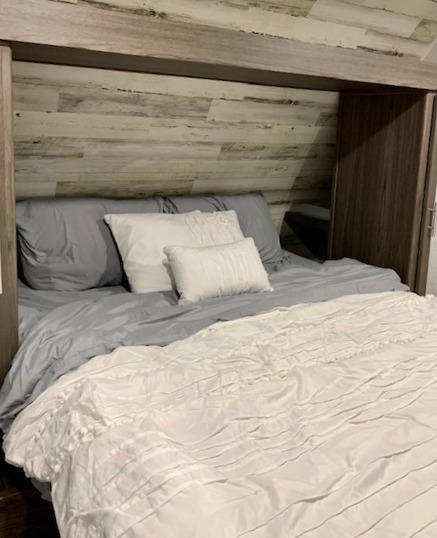 Cozy RV rental bedroom with rustic wood paneling, crisp white bedding, & built-in storage.. Dutchmen Other 2021