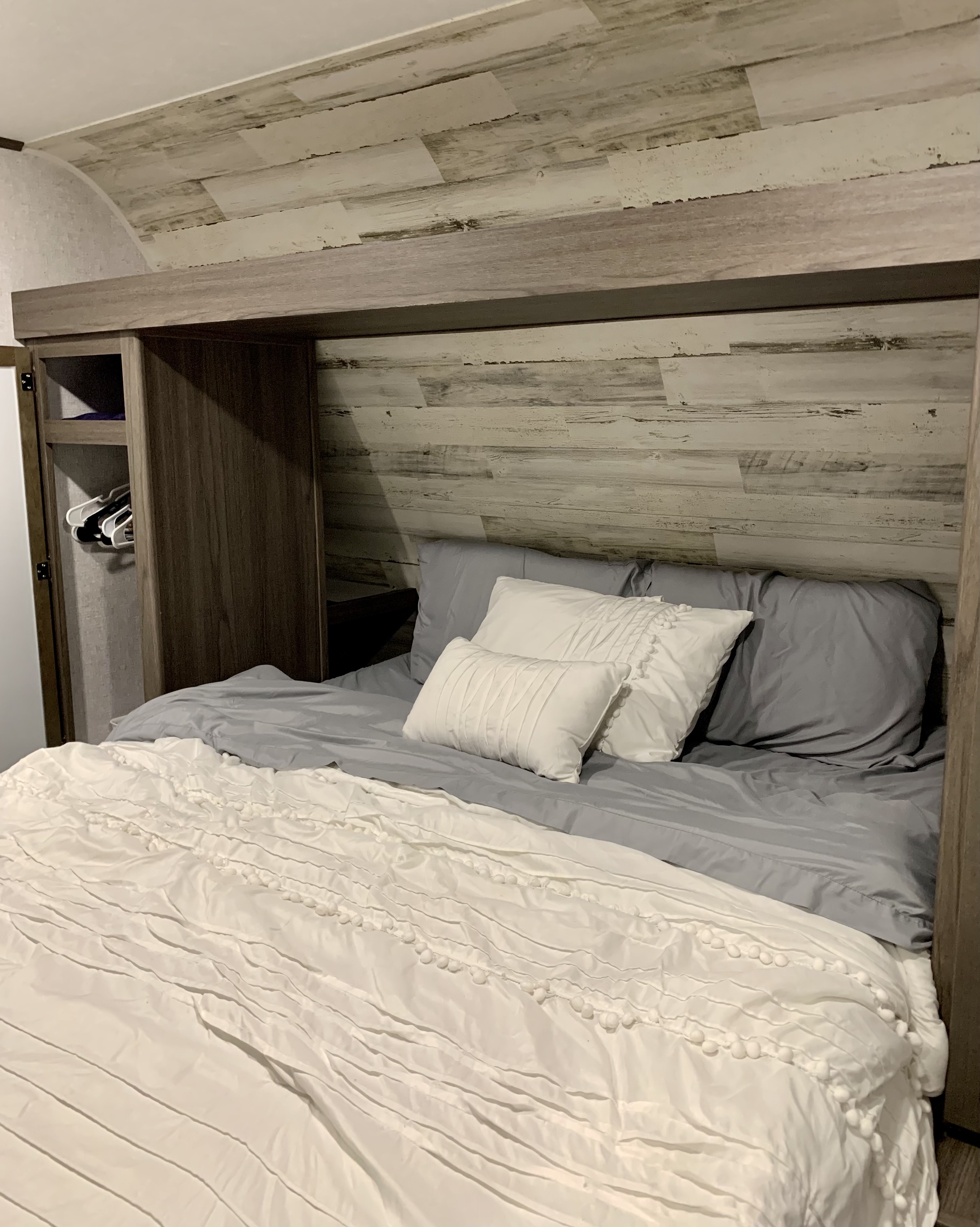 Cozy RV rental bedroom: light wood-paneled walls, gray sheets, white duvet with bobbles, built-in wardrobe.. Dutchmen Other 2021