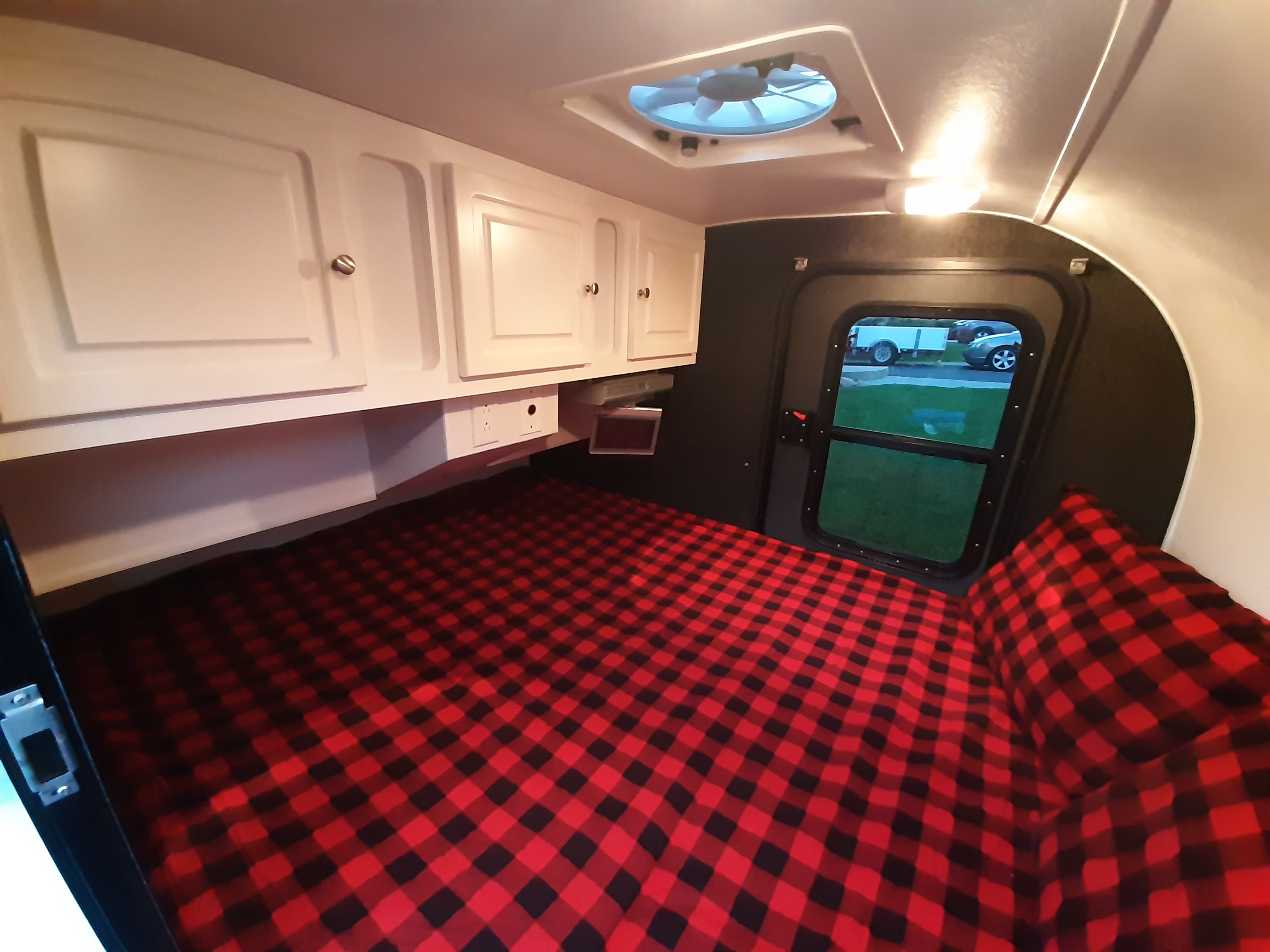 Cozy RV rental interior: red plaid bed, overhead cabinets, and a window view in a compact camper. Ready for adventure!. Little Guy Little Guy Trailer 2011