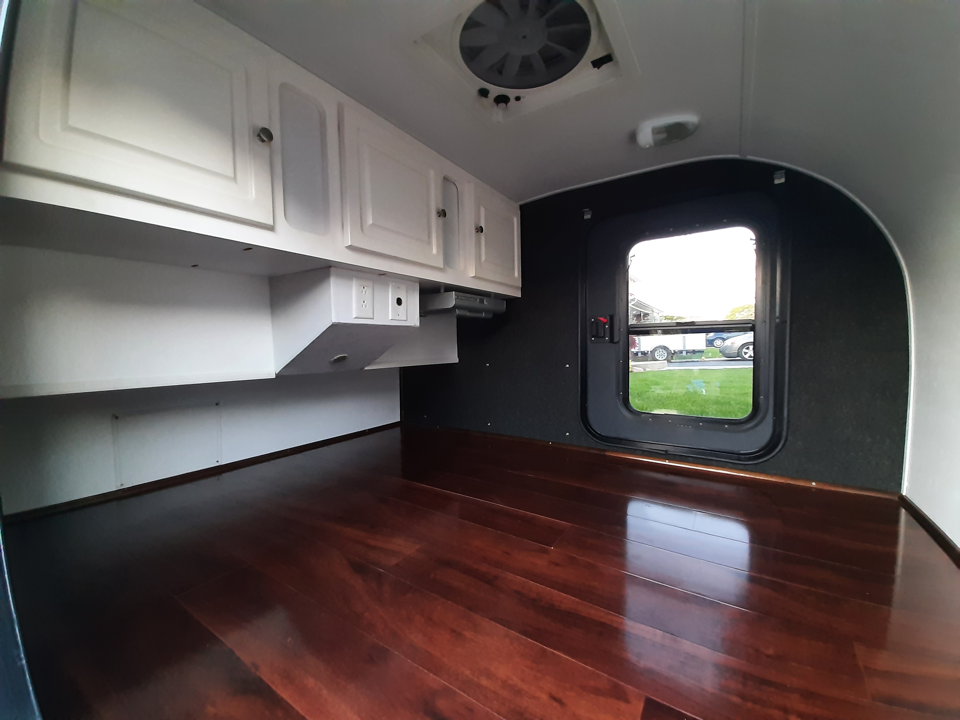 Inside an RV rental: bright white cabinets, polished wood floor, a ceiling vent, and a window for outdoor views.. Little Guy Little Guy Trailer 2011