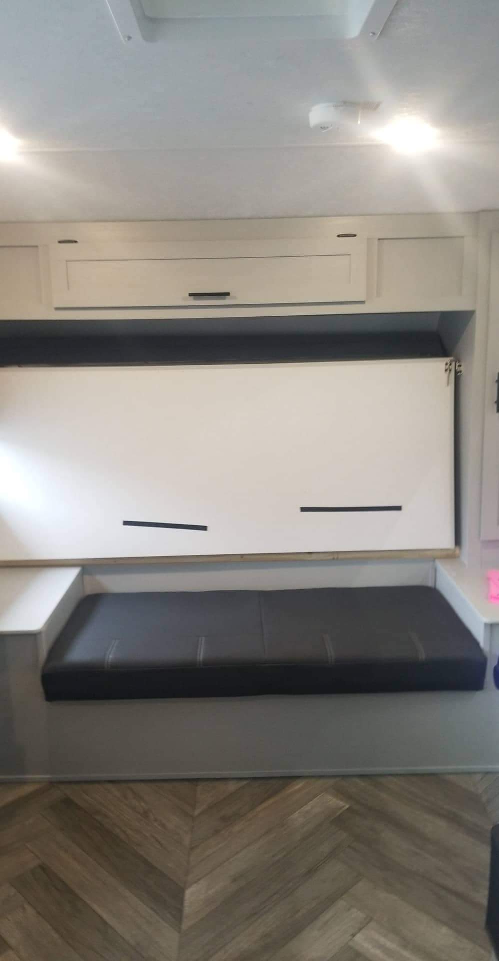 RV rental interior featuring a versatile sofa and fold-down bunk bed, overhead cabinets, and stylish herringbone flooring.. Forest River Wildwood 2021