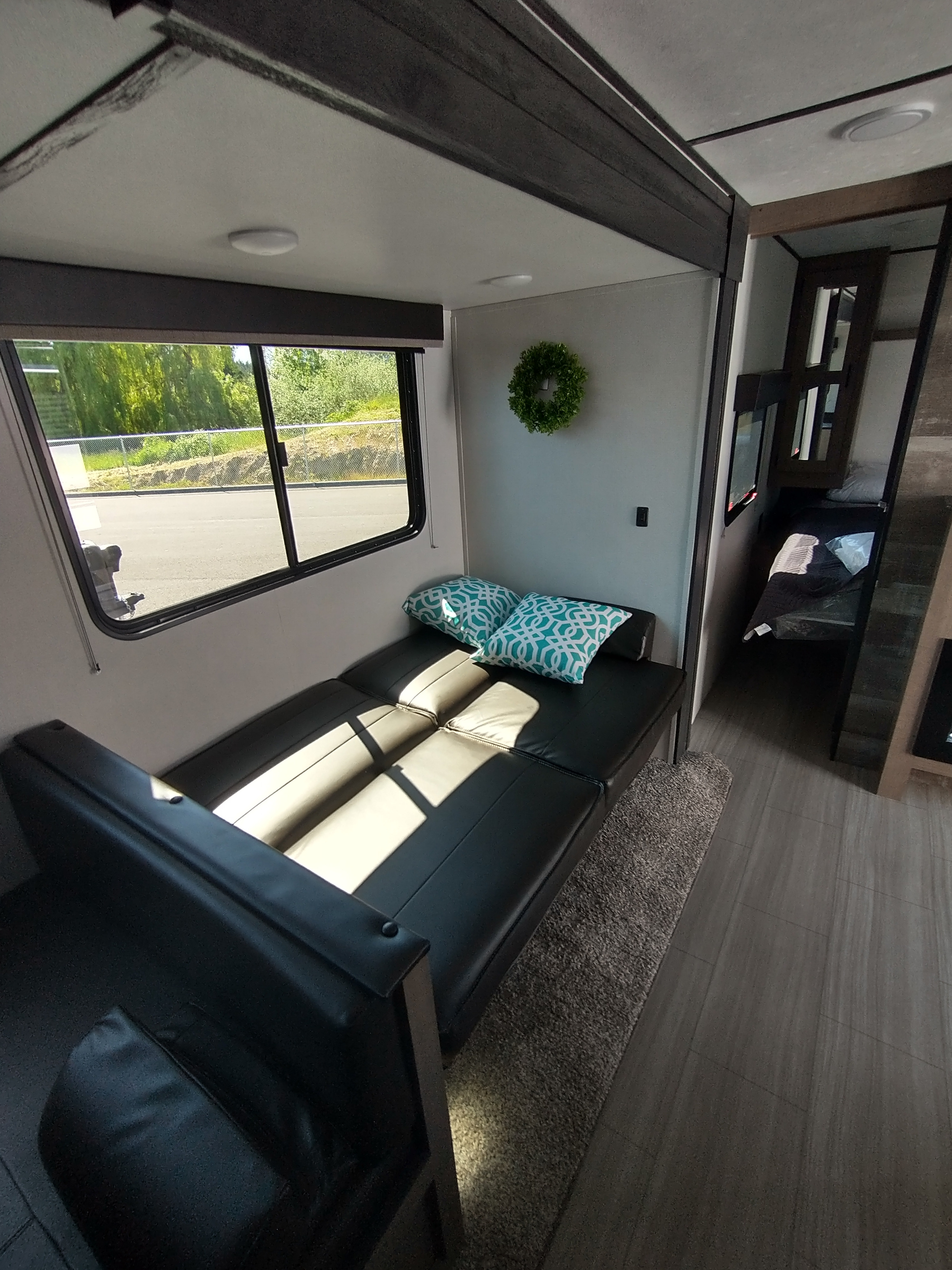 Bright RV rental interior showing a modern black sofa bed, teal pillows, and a window with a scenic view outside.. Keystone Other 2021