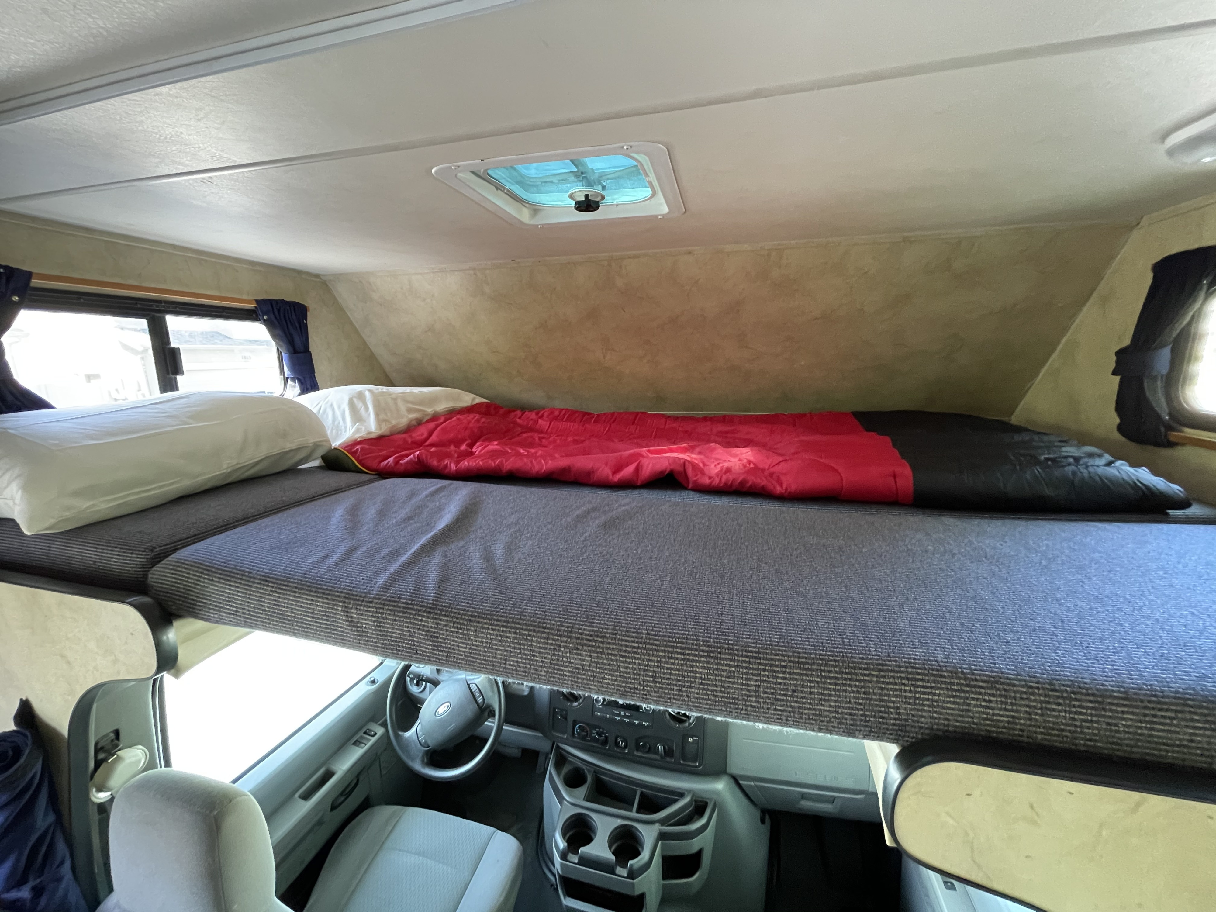 Sleep area of an RV rental with bed, pillows, and sleeping bag above the driver's cabin. Perfect for road trips.. Thor Thor Motorhome 2012