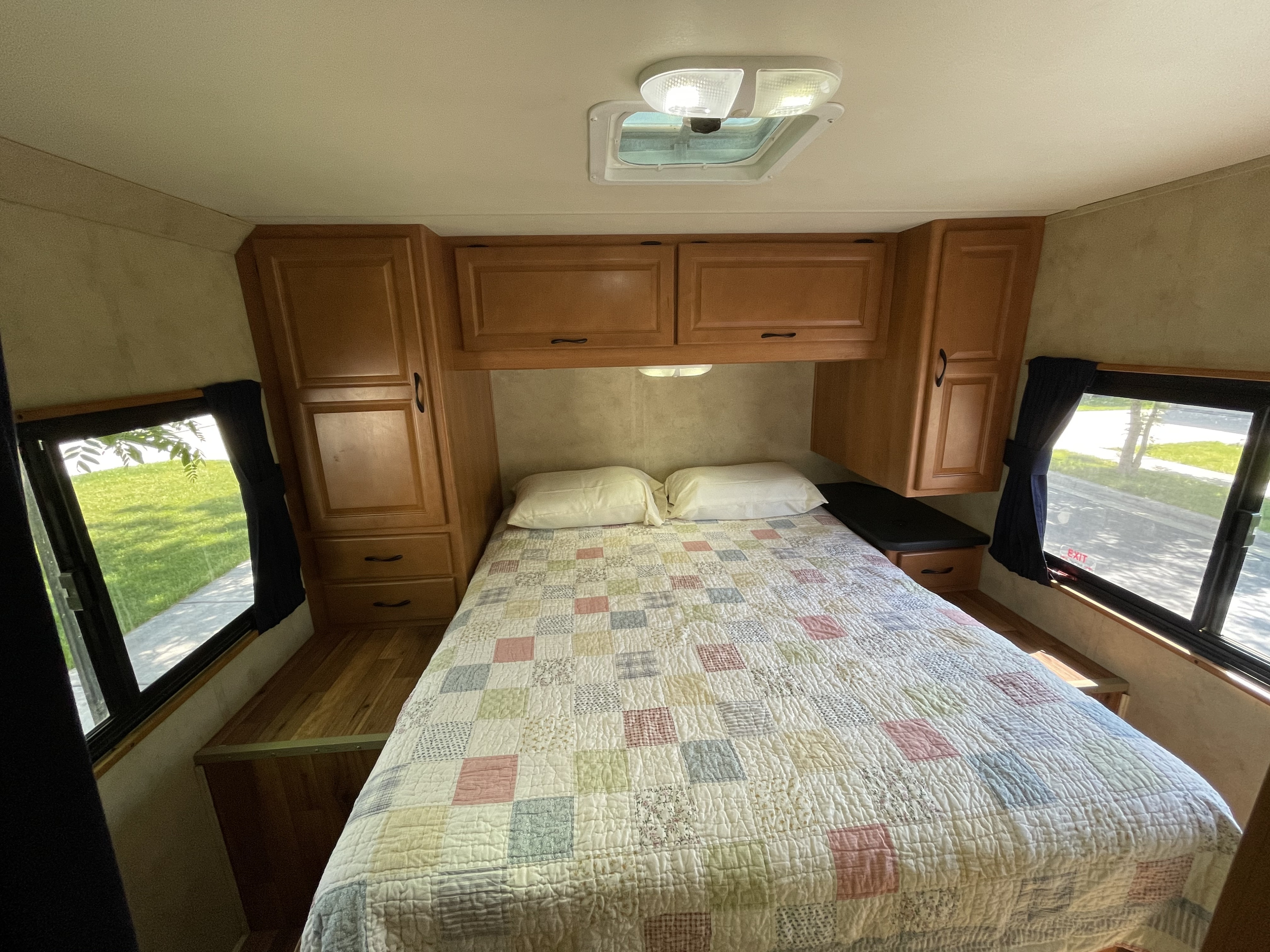 RV rental bedroom interior, showcasing a cozy bed, wooden cabinets, and windows with scenic outdoor views.. Thor Thor Motorhome 2012
