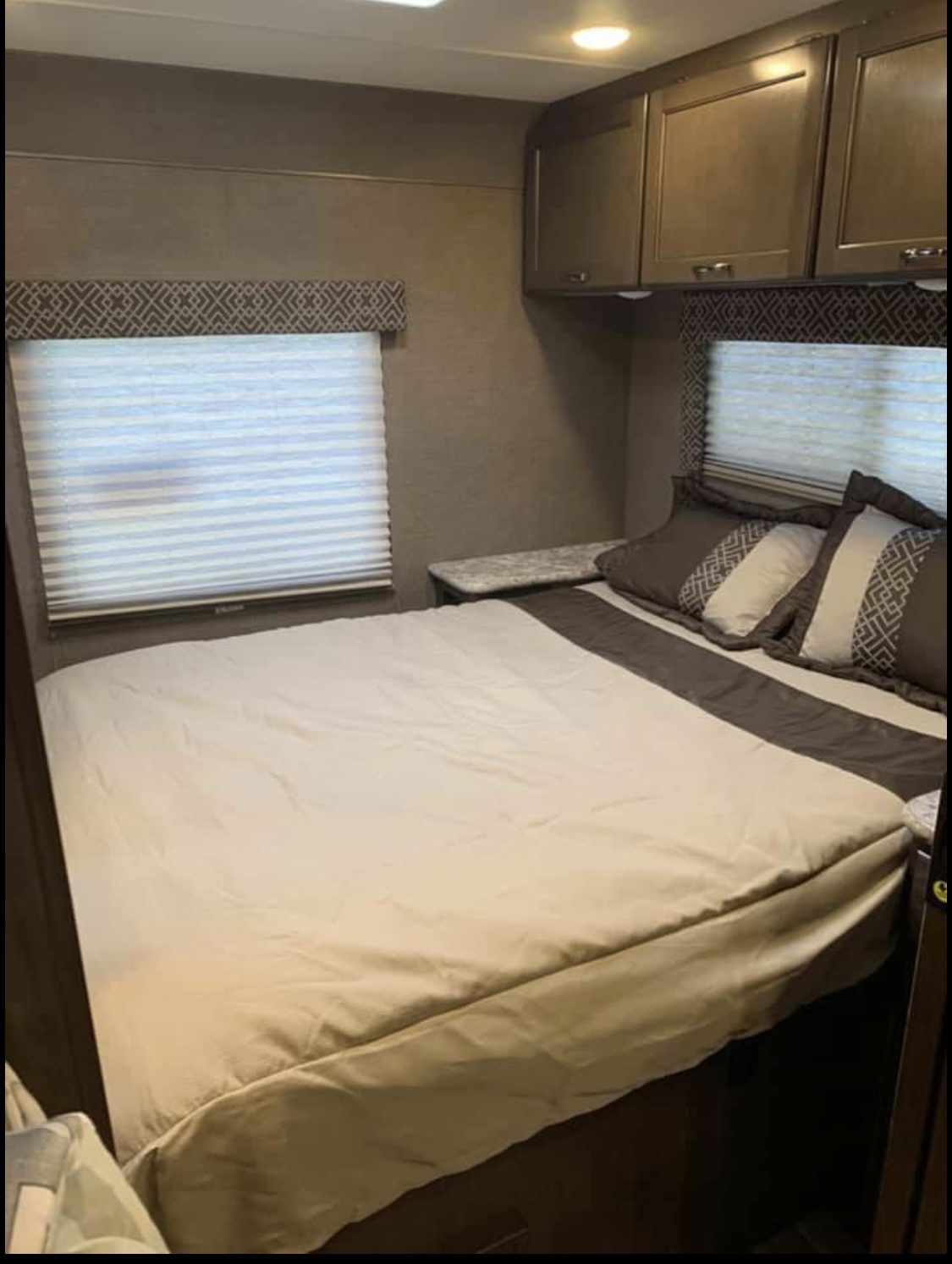 An RV rental bedroom featuring a large bed, blinds on windows, and overhead cabinets for a comfortable stay.. Thor Motor Coach Four Winds 2019