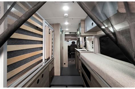 RV rental interior: cozy camper van with wood-slat bed, compact kitchen, and front cab view. Ready for adventure.. Winnebago Solis 2021