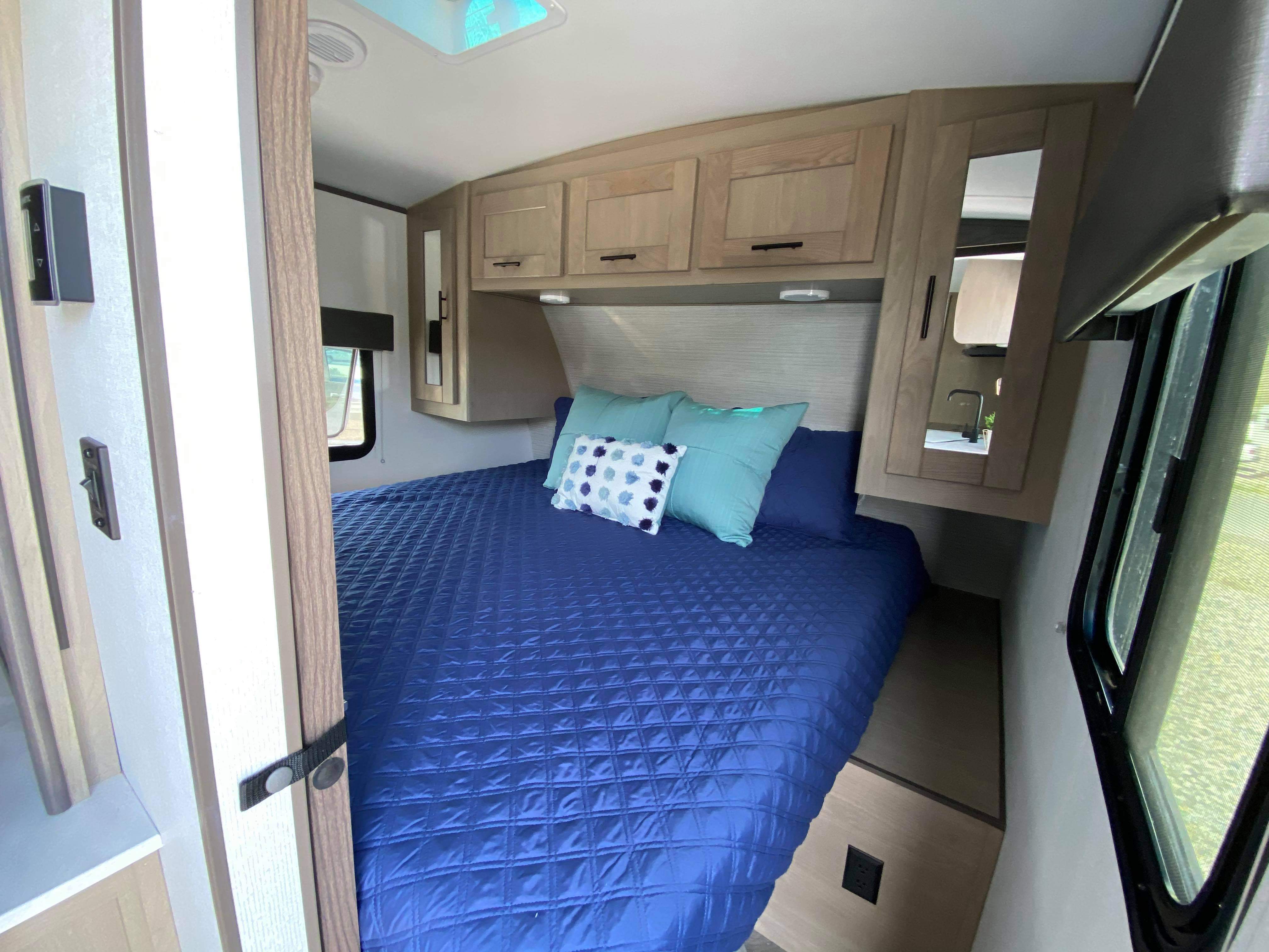 RV rental bedroom: a comfortable blue bed with pillows, overhead cabinets for storage, and windows for natural light and views.. Cruiser Rv Corp Shadow Cruiser 2021