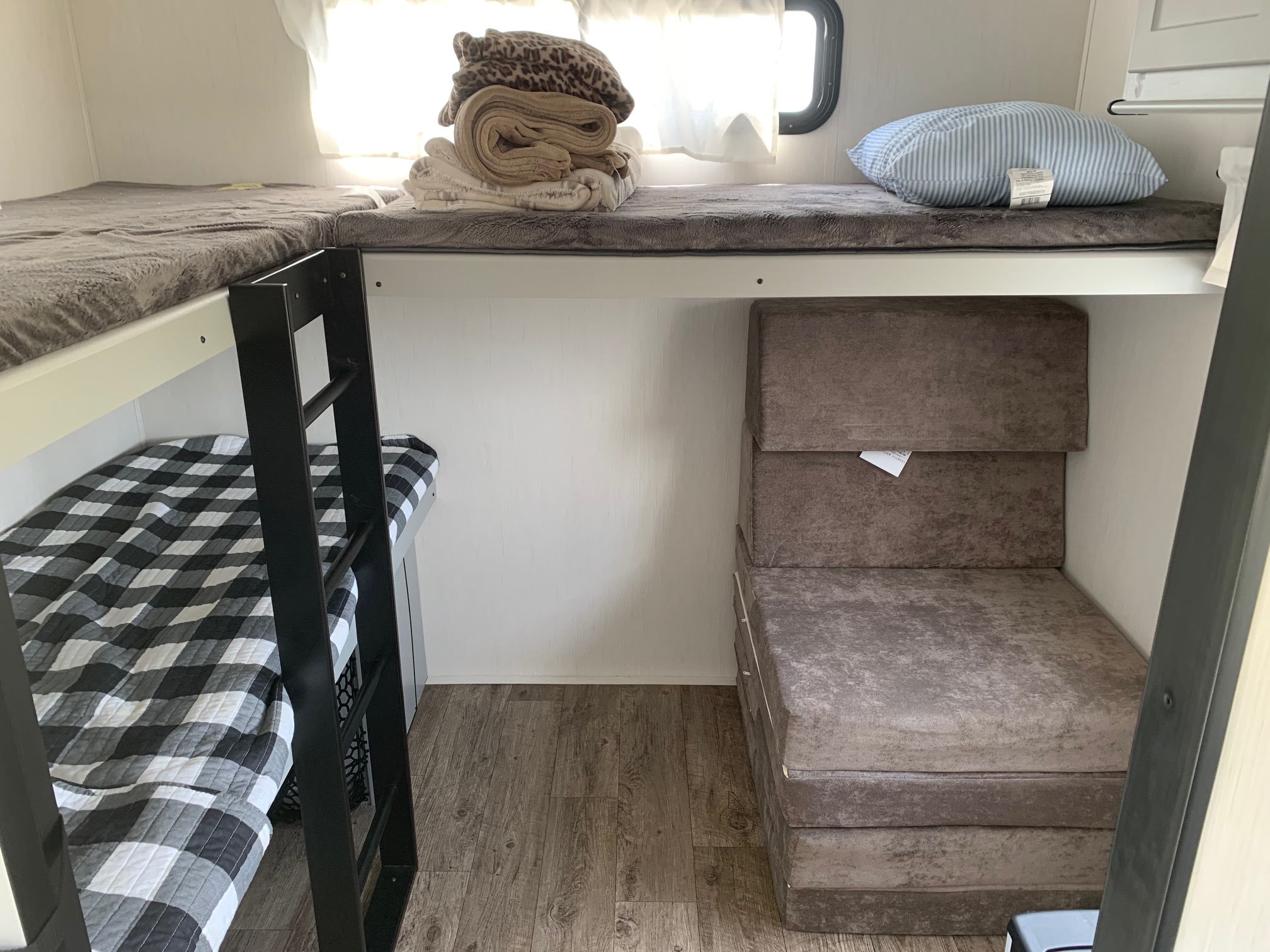 RV rental interior: lower bunk bed with plaid quilt, upper bunks with gray pads & blankets, and a brown modular sofa/bed unit.. Forest River Vibe 2021
