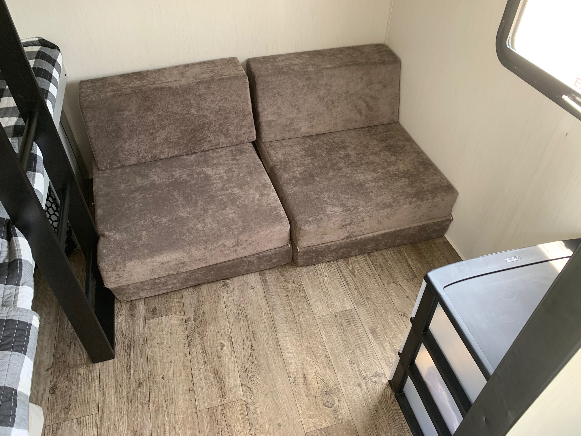 Cozy RV rental interior with adaptable gray seating, bunk bed, wood-look floor, and plastic storage unit.. Forest River Vibe 2021