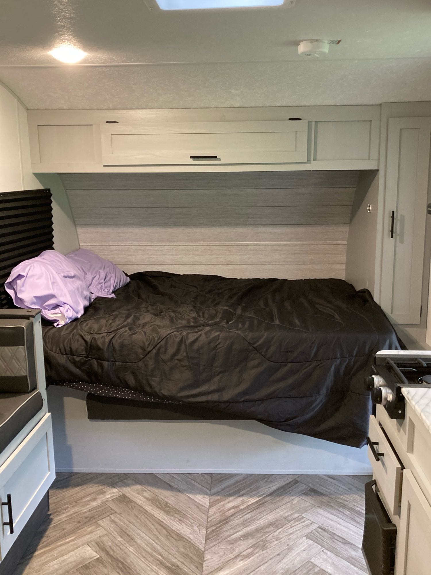 Cozy RV rental interior with a comfortable bed, ample overhead storage, and kitchen area visible, featuring patterned flooring.. Forest River Wildwood 2021