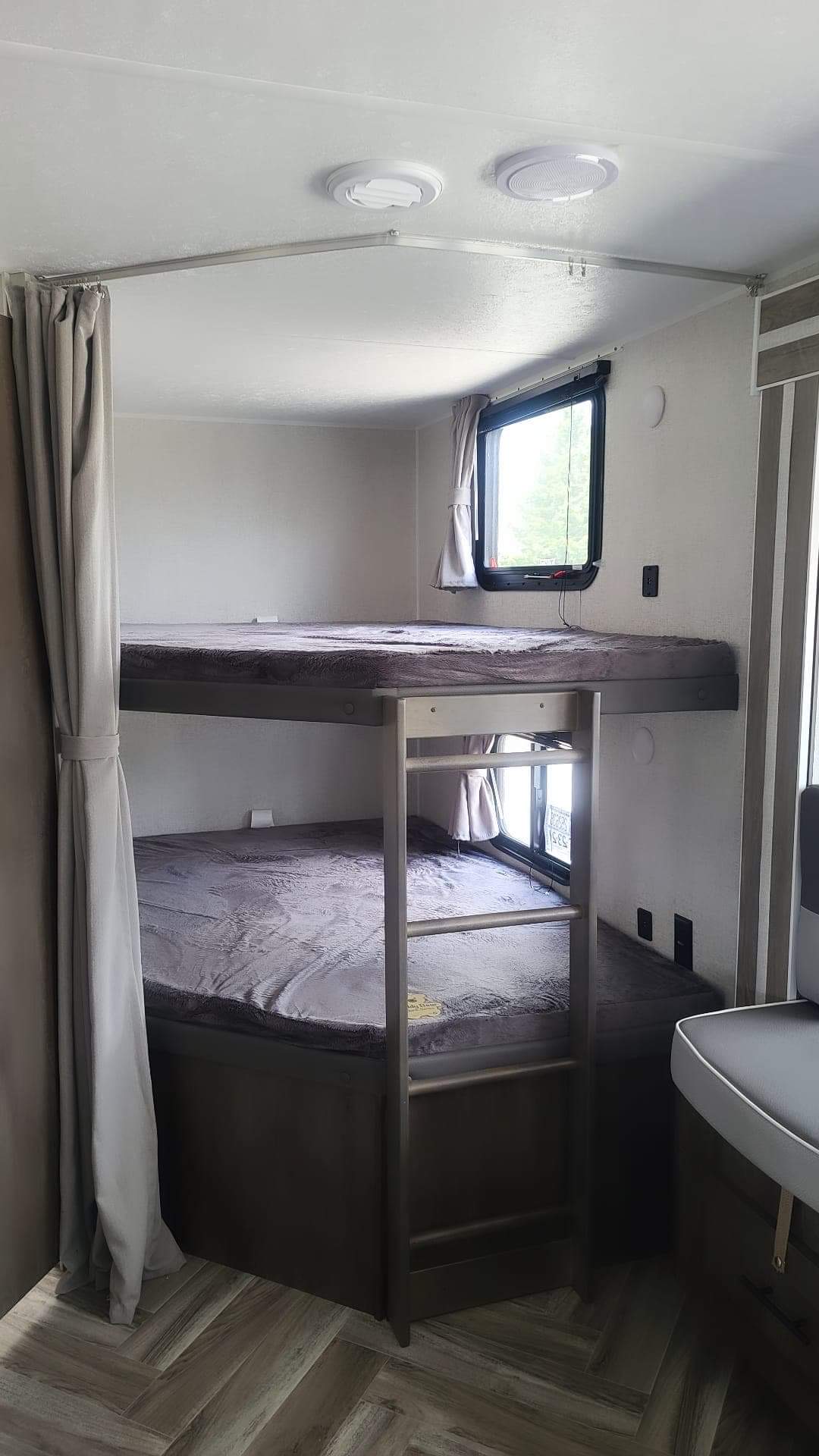 Cozy RV rental interior featuring comfortable bunk beds with windows and a privacy curtain, ideal for compact family sleeping.. Forest River Salem Cruise Lite 2021