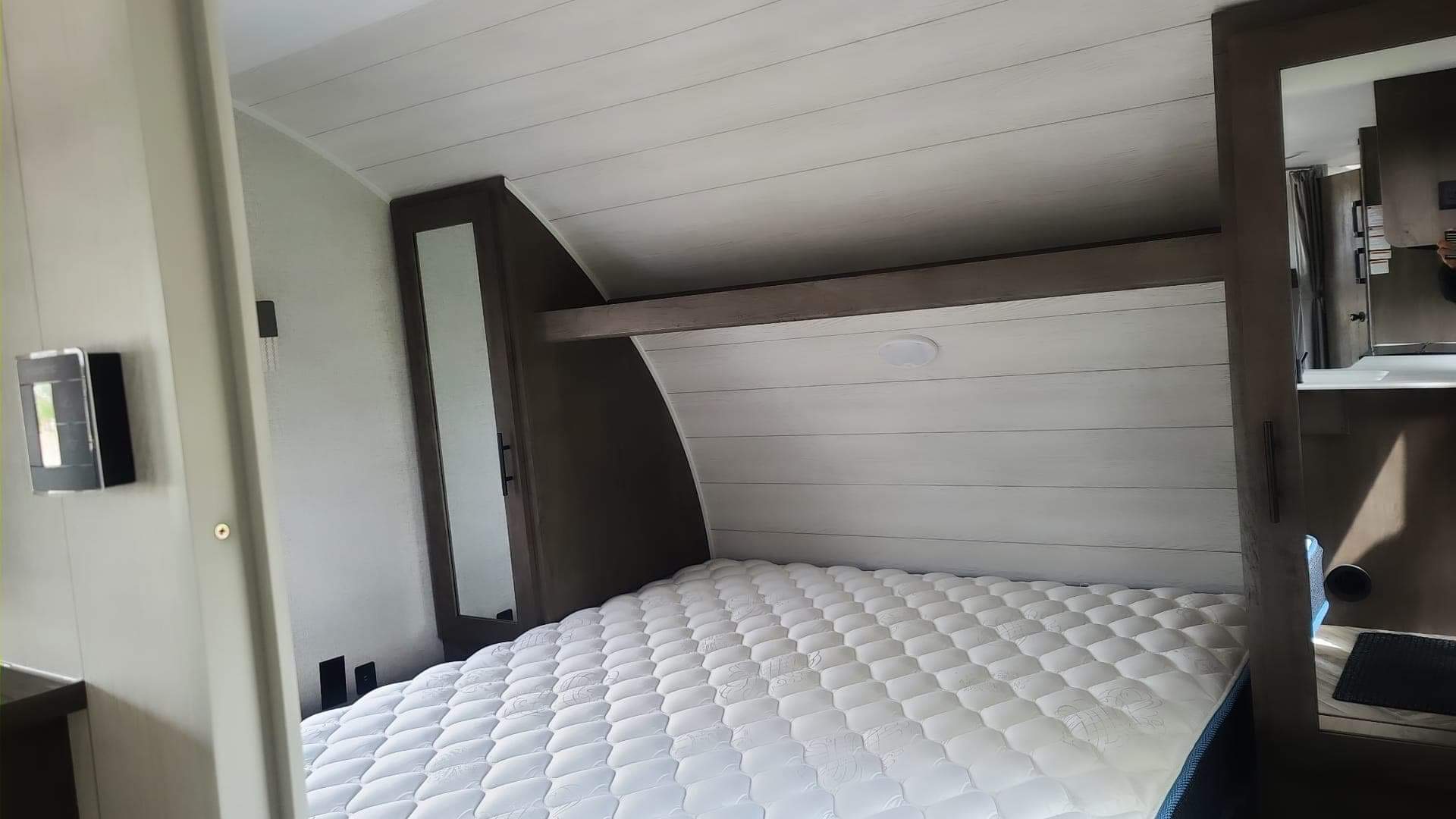 Inside a clean RV rental: a compact bedroom with a white mattress, shiplap ceiling, and built-in storage.. Forest River Salem Cruise Lite 2021