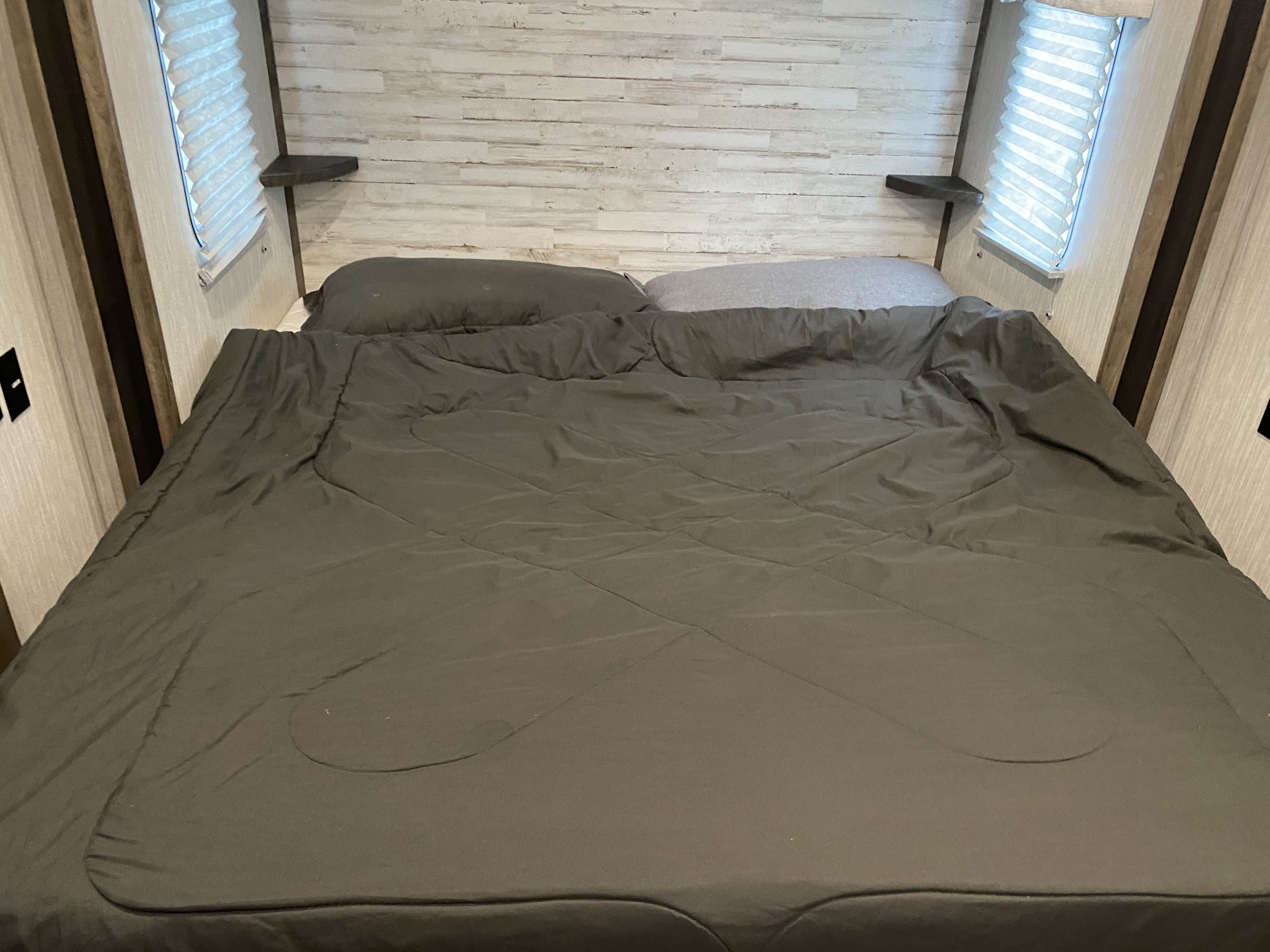 Cozy RV rental bedroom featuring a comfortable bed, wood-paneled headboard, and side windows with blinds.. Forest River Sabre 2020