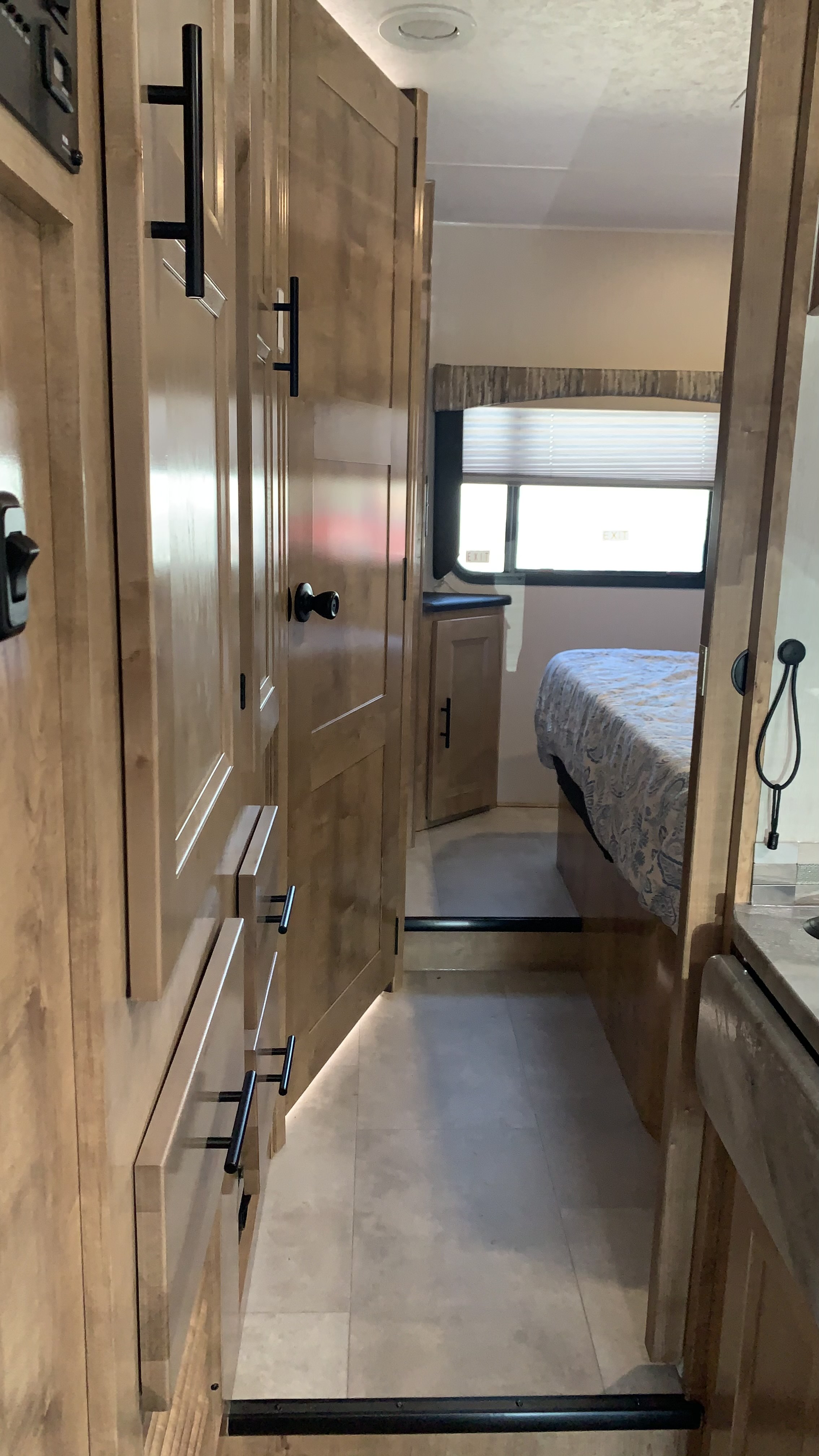 RV rental interior: Clean, light wood hallway with cabinets, stepping down to a bedroom with window and bed.. Coachmen Leprechaun 2020