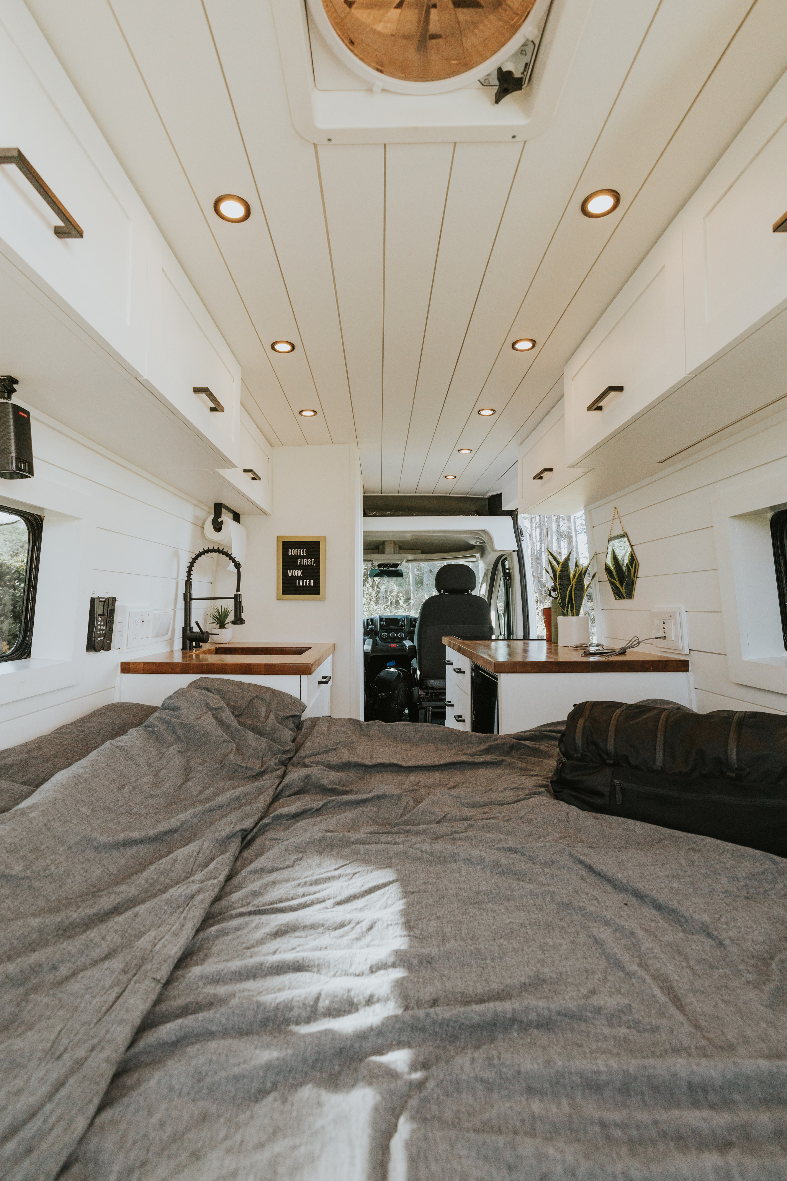 Inside a bright RV rental: features a comfy bed with grey bedding, a full kitchen area with a sink, and sleek storage solutions.. Ram Promaster 2500 2019
