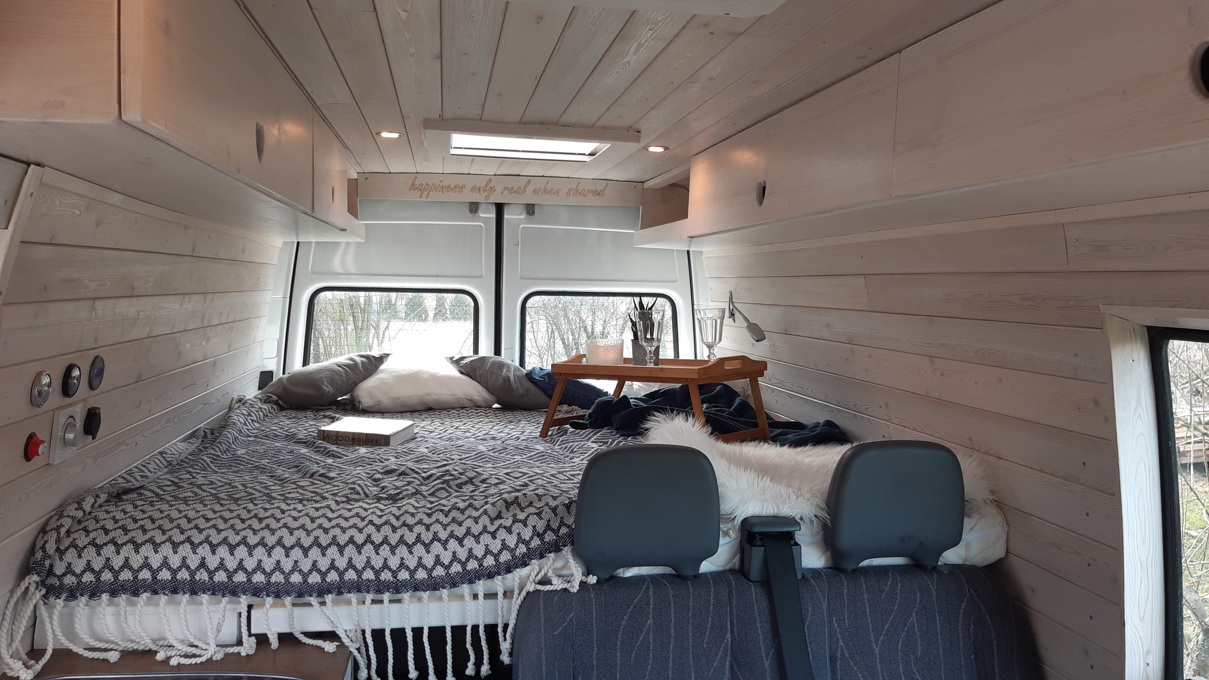 Bright, cozy RV rental interior: wood-paneled walls, large bed, and scenic rear windows for travel.. Mercedes-Benz Sprinter 2001