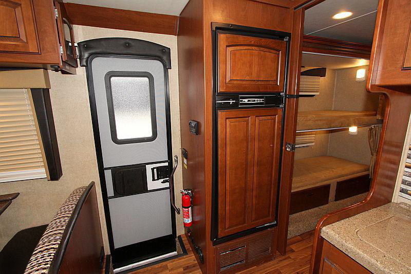 This RV rental interior showcases a compact kitchen with fridge, main entry door, dining booth, and rear bunk beds for travel.. Jayco Greyhawk 2015