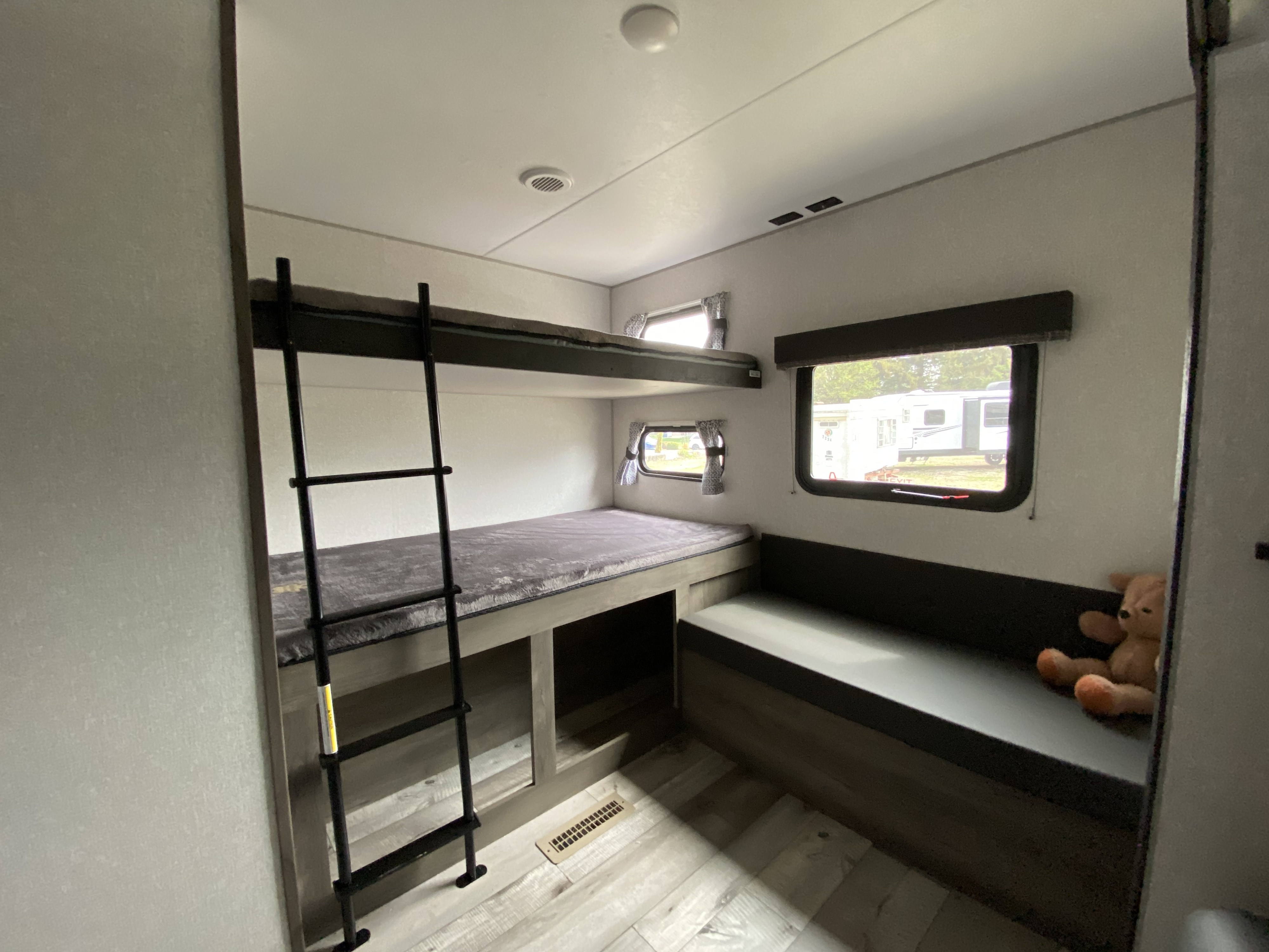 Cozy RV rental interior showing bunk beds with ladder, a long bench seat, and windows with outdoor views.. Sportsmen LE 2021