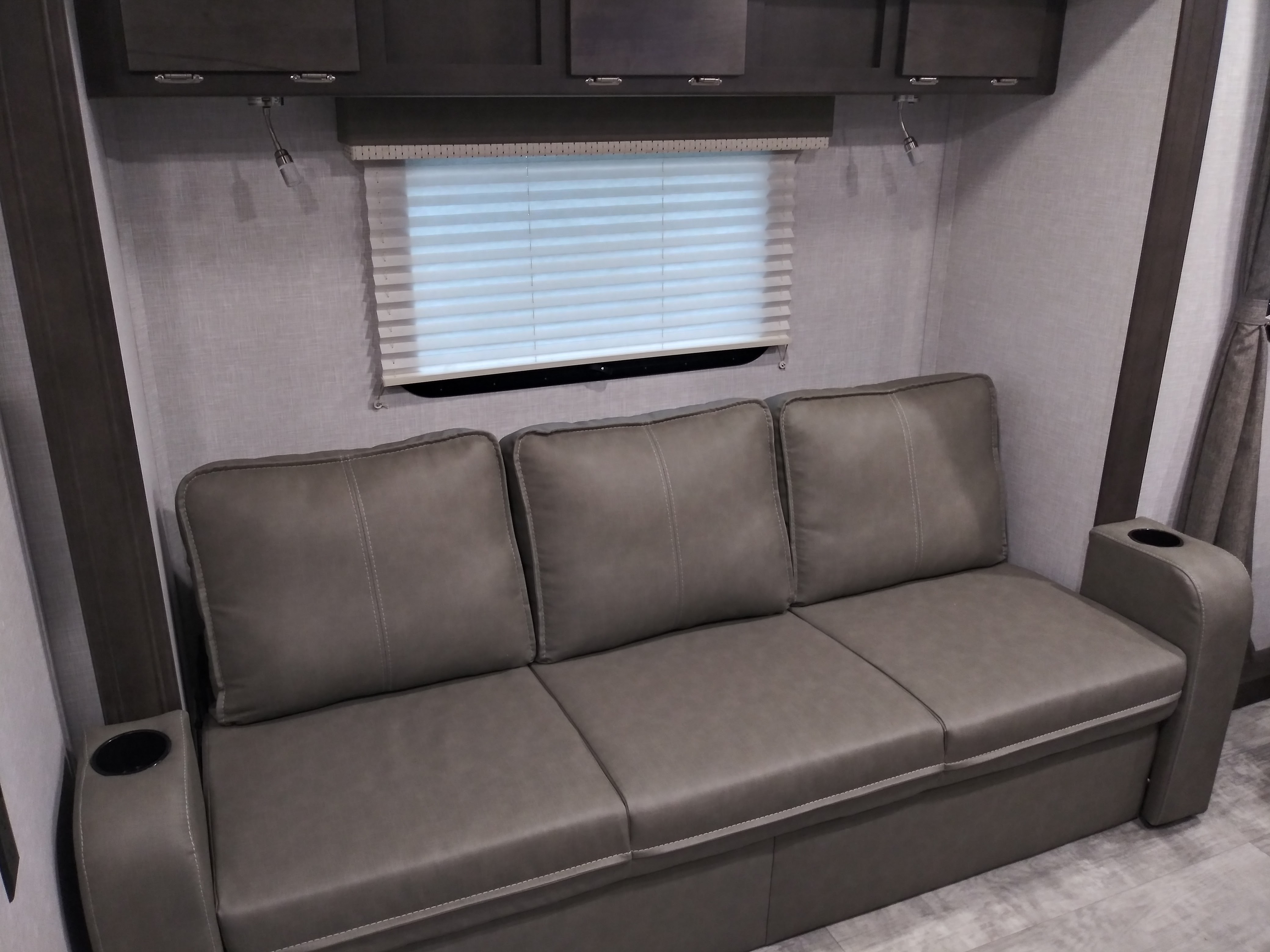 RV rental interior: cozy gray sofa with cup holders, window, and overhead storage cabinets, perfect for relaxing.. Forest River Rockwood Mini Lite 2021
