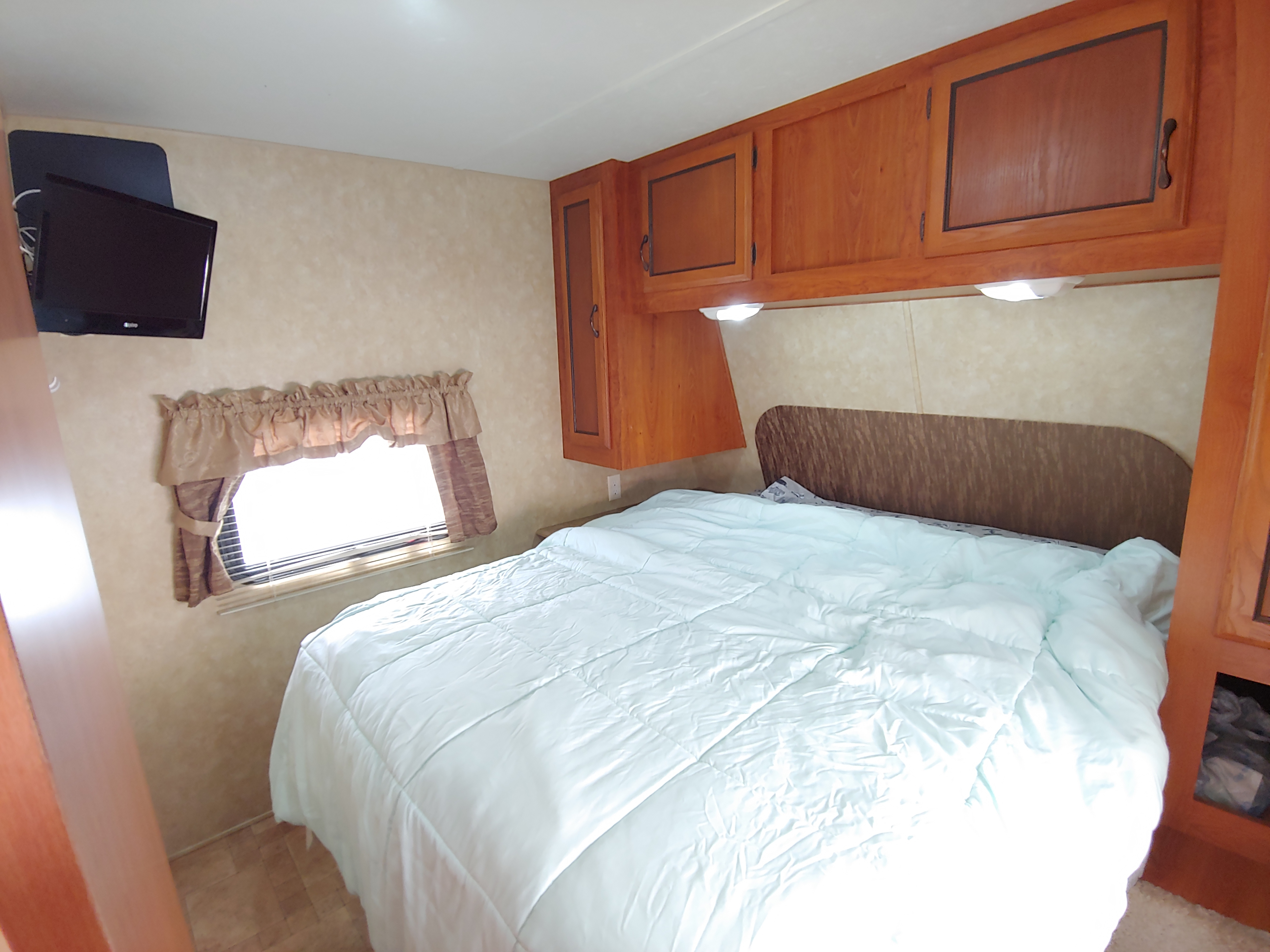 Cozy RV rental bedroom featuring a comfy bed, overhead storage cabinets, wall-mounted TV, and a window.. Coachmen Catalina 2011