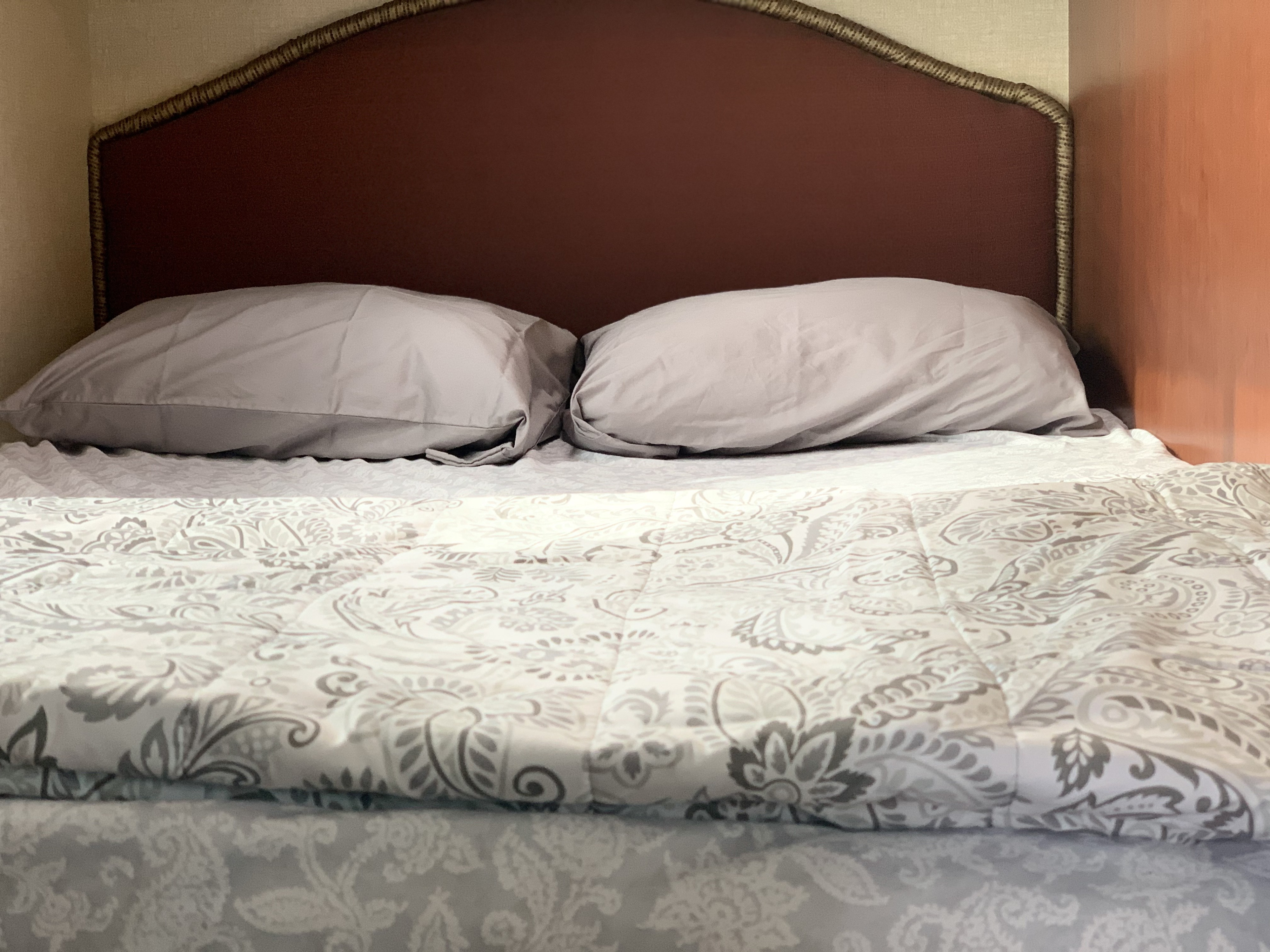 Cozy RV rental bedroom features a patterned bedspread, grey pillows, and brown headboard for travel comfort.. Winnebago Minnie Winnie 2015